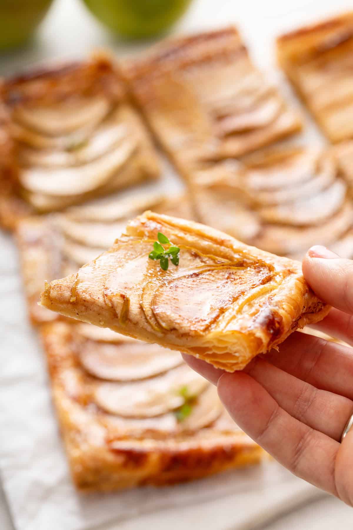 Hand holding up a slice of puff pastry apple tart.