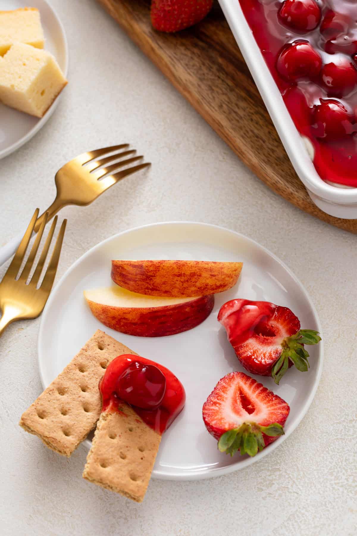 Apple slices, strawberries, and graham crackers on a white plate with cherry cheesecake dip.