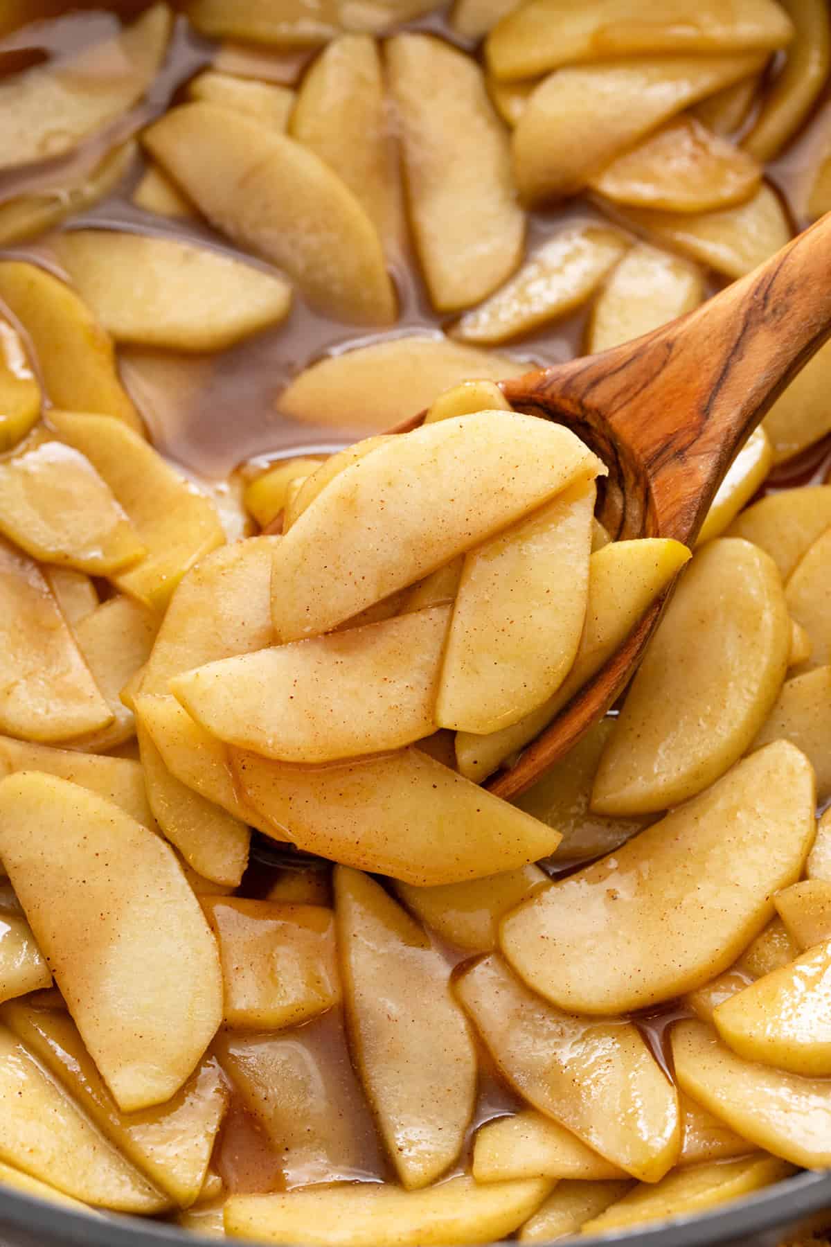 Wooden spoon holding up a spoonful of sauteed apples in a pan.