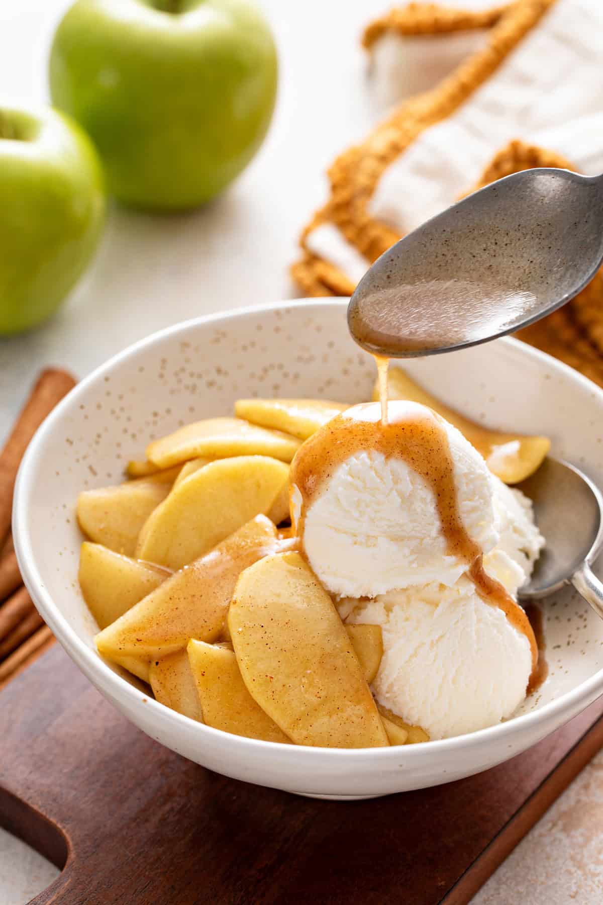 Spoon pouring the sauce from sauteed apples over vanilla bean ice cream.