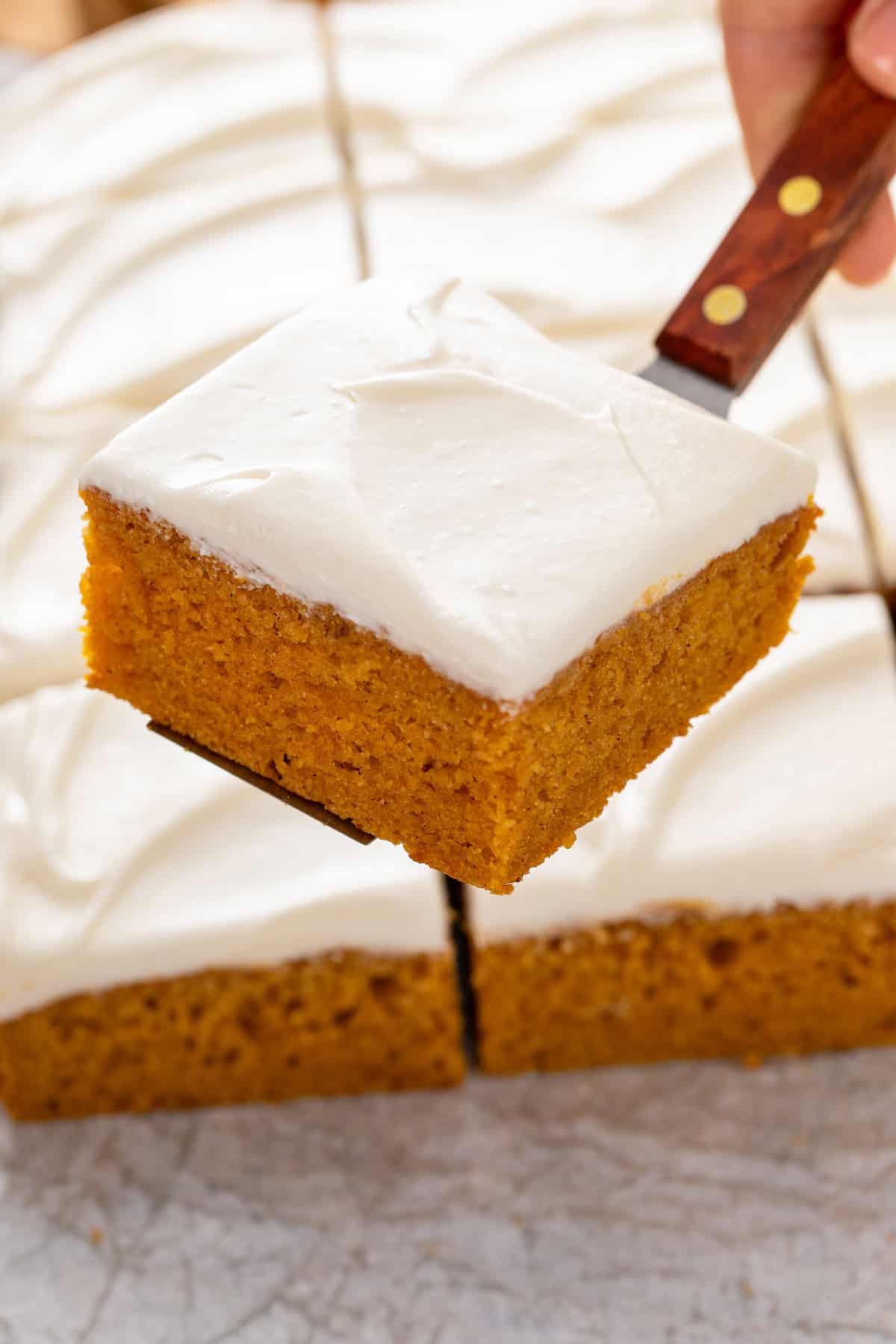 Spatula holding up a pumpkin bar with cream cheese frosting.