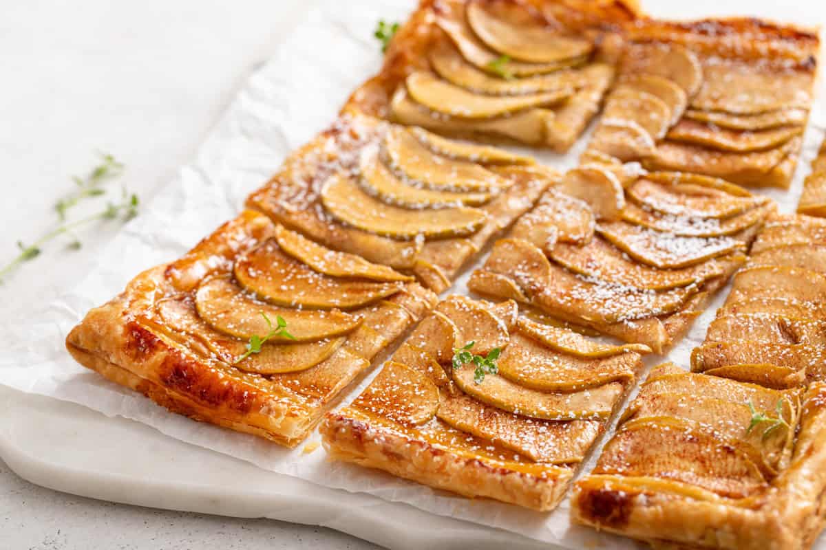 Sliced puff pastry apple tart on a marble board.