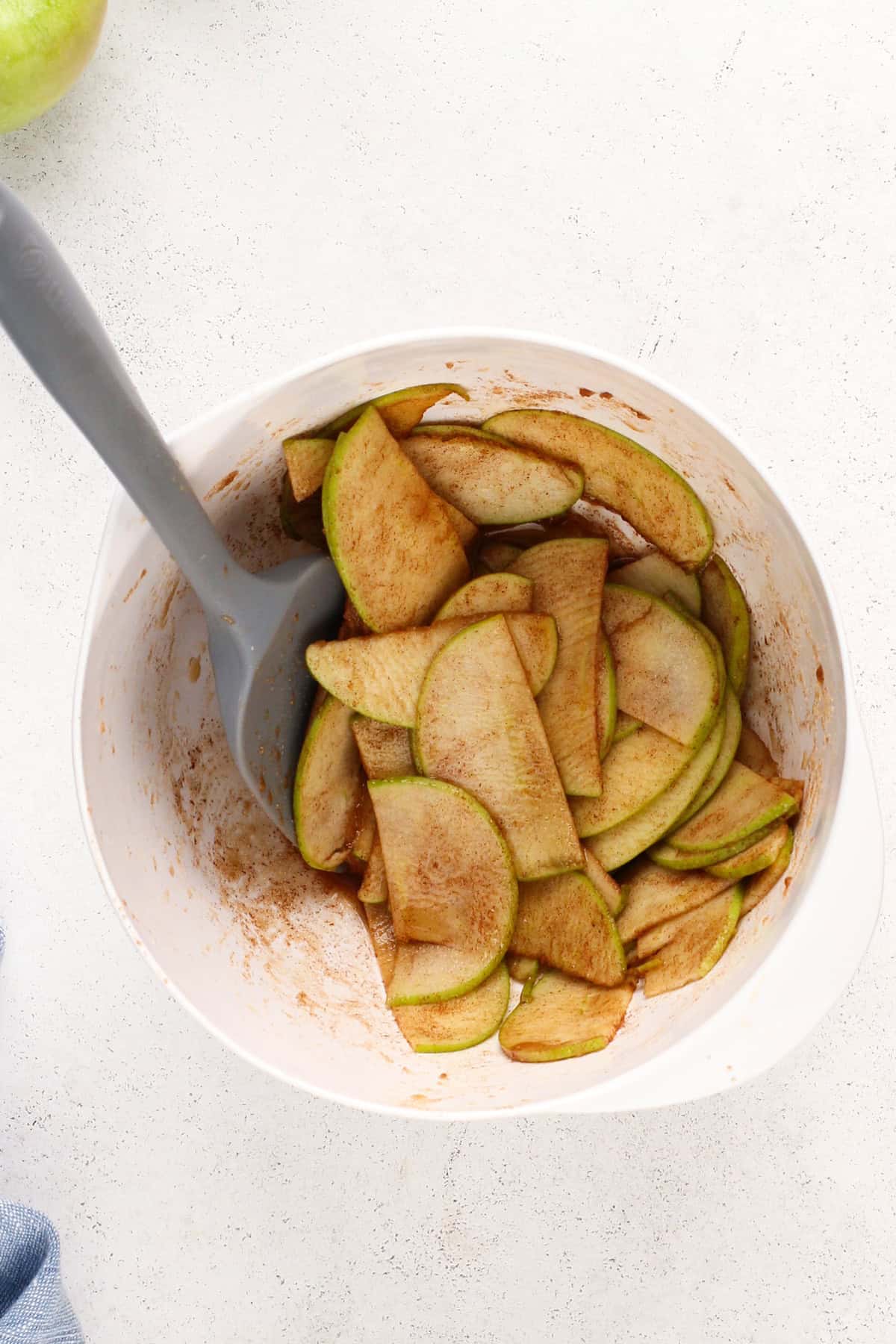 Apple slices tossed with spices in a white bowl.