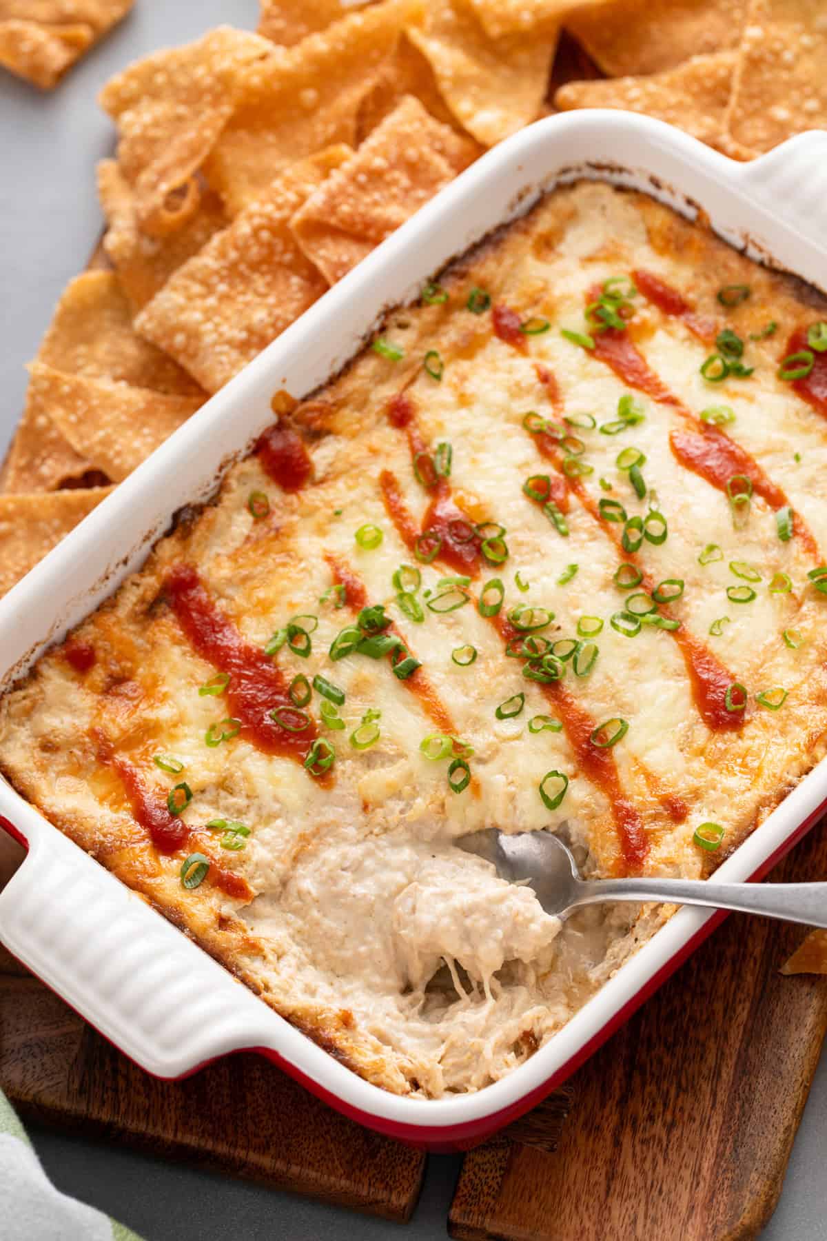 Spoon in the corner of a baking dish filled with crab rangoon dip.