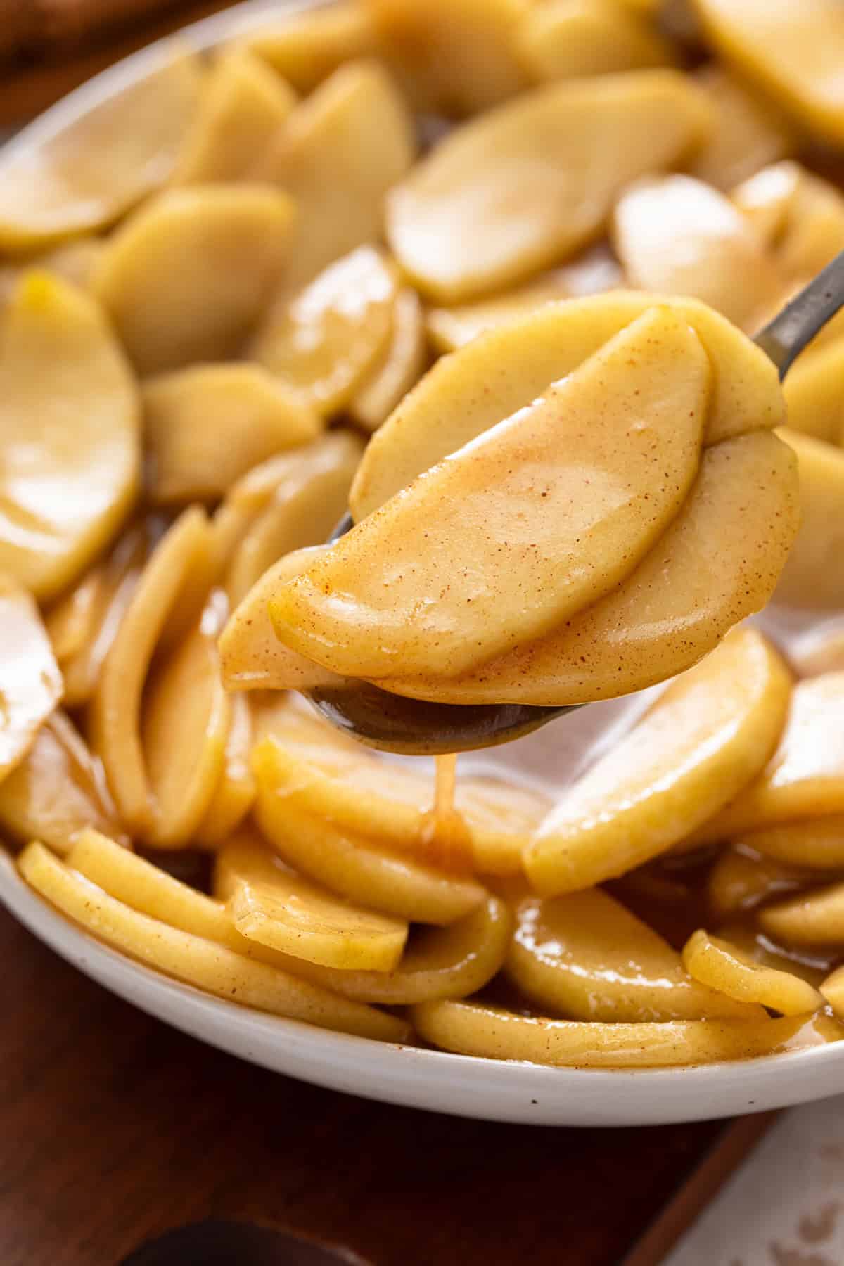 Spoon scooping up a portion of sauteed apples from a bowl.