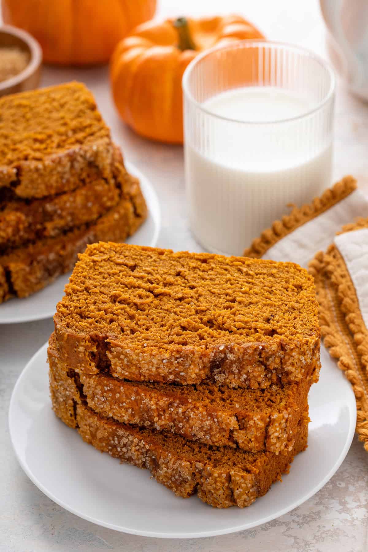 Three slices of 2-ingredient pumpkin bread stacked on a white plate in front of a glass of milk.