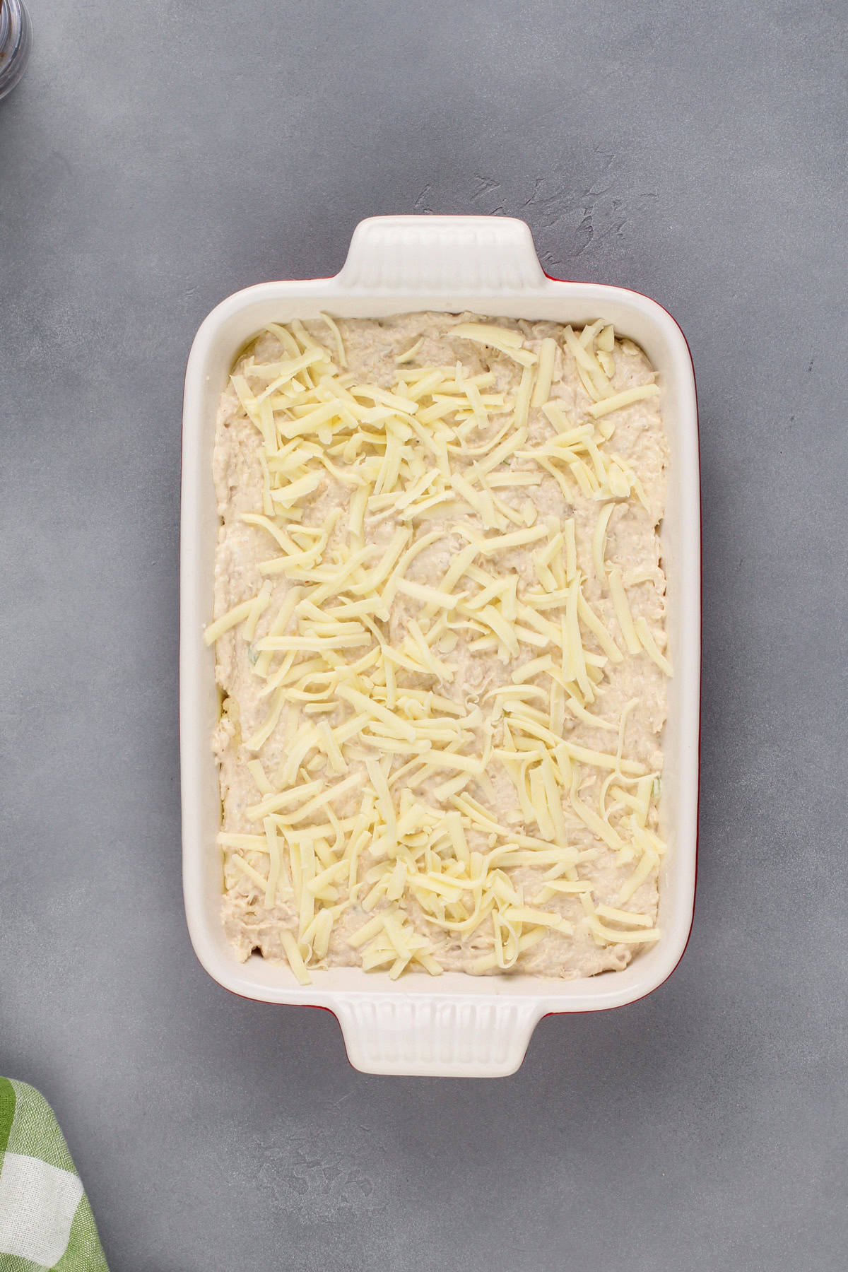 Unbaked crab rangoon dip in a baking dish, topped with shredded cheese.