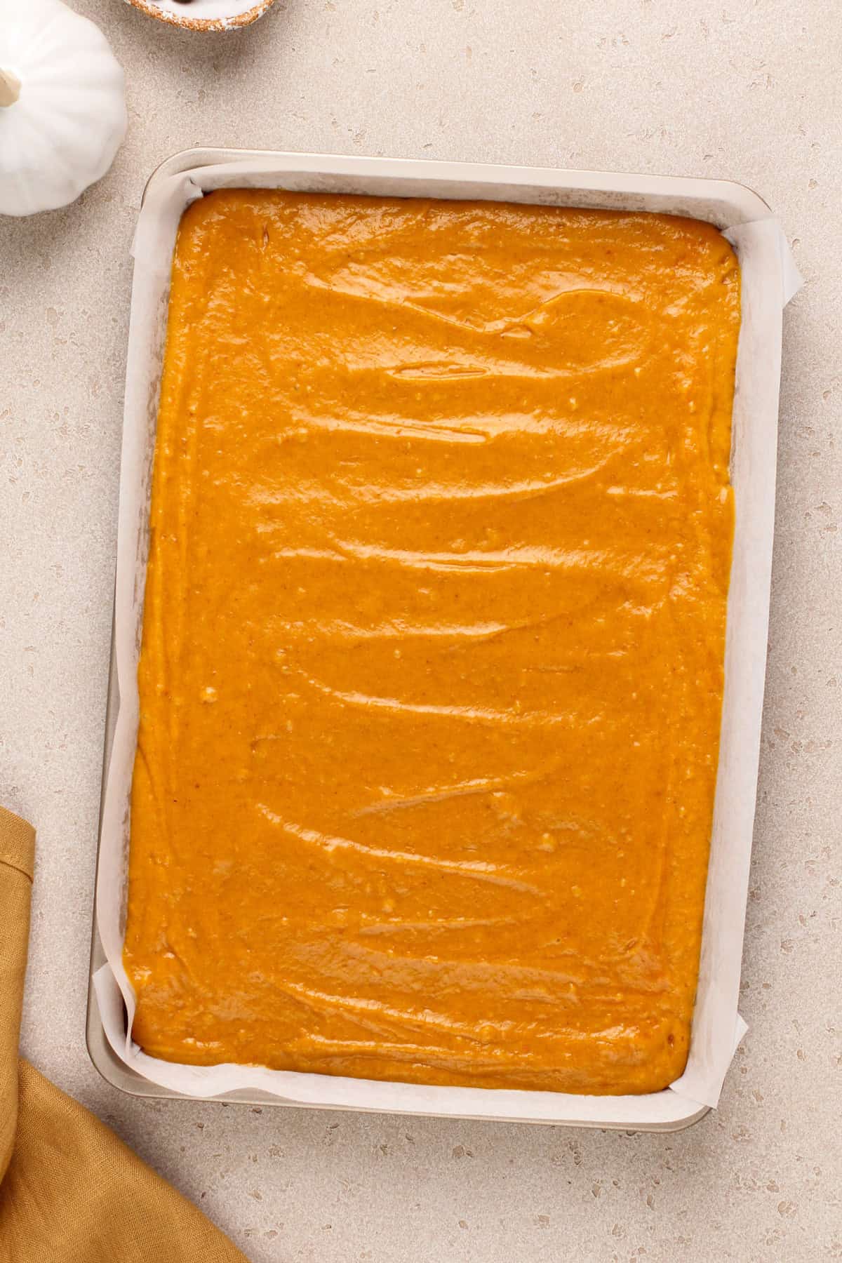 Batter for pumpkin bars spread into a jelly roll pan, ready to go in the oven.