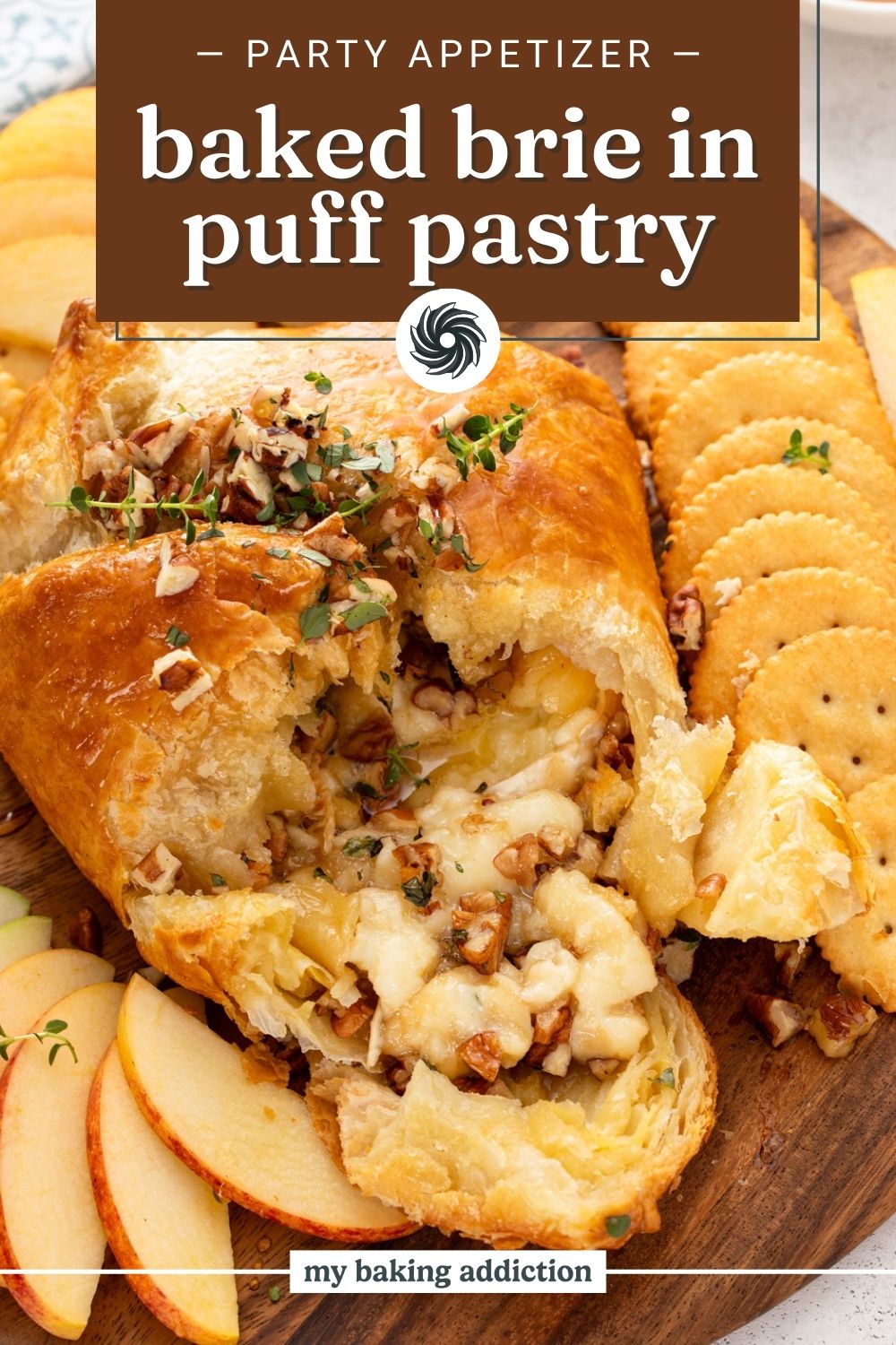 Baked brie in puff pastry that has been cut into surrounded by apple slices and crackers. Text overlay includes recipe name.