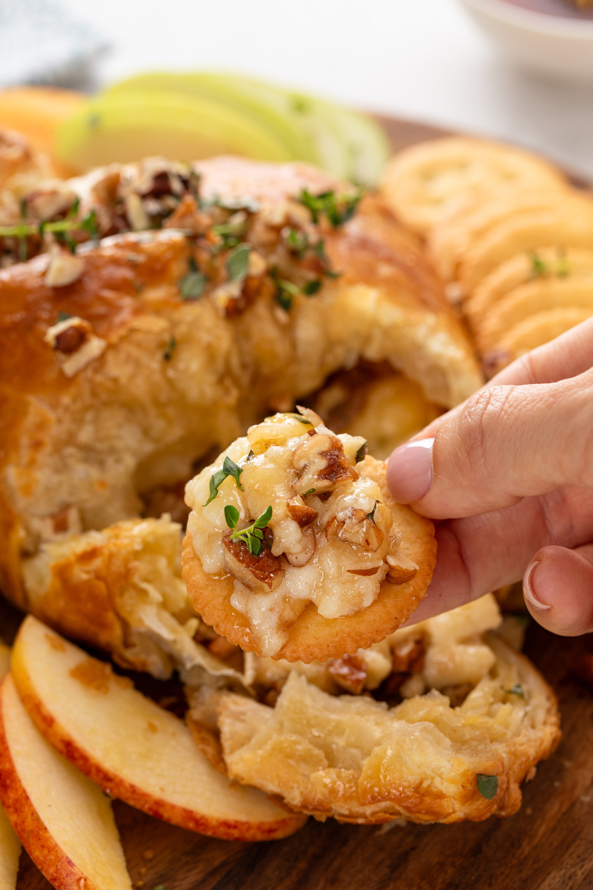 Hand holding a cracker with baked brie on it.