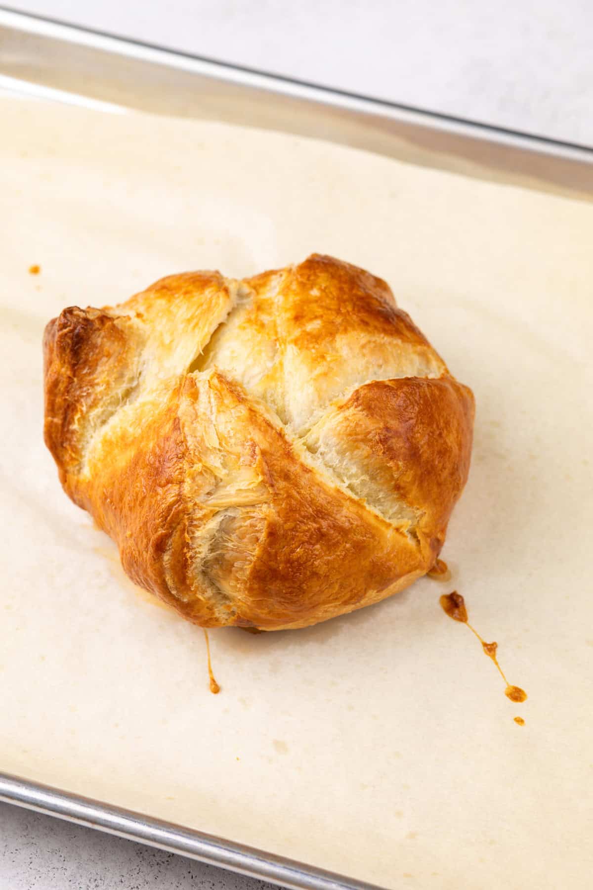 Baked brie in puff pastry cooling on a parchment-lined baking sheet.