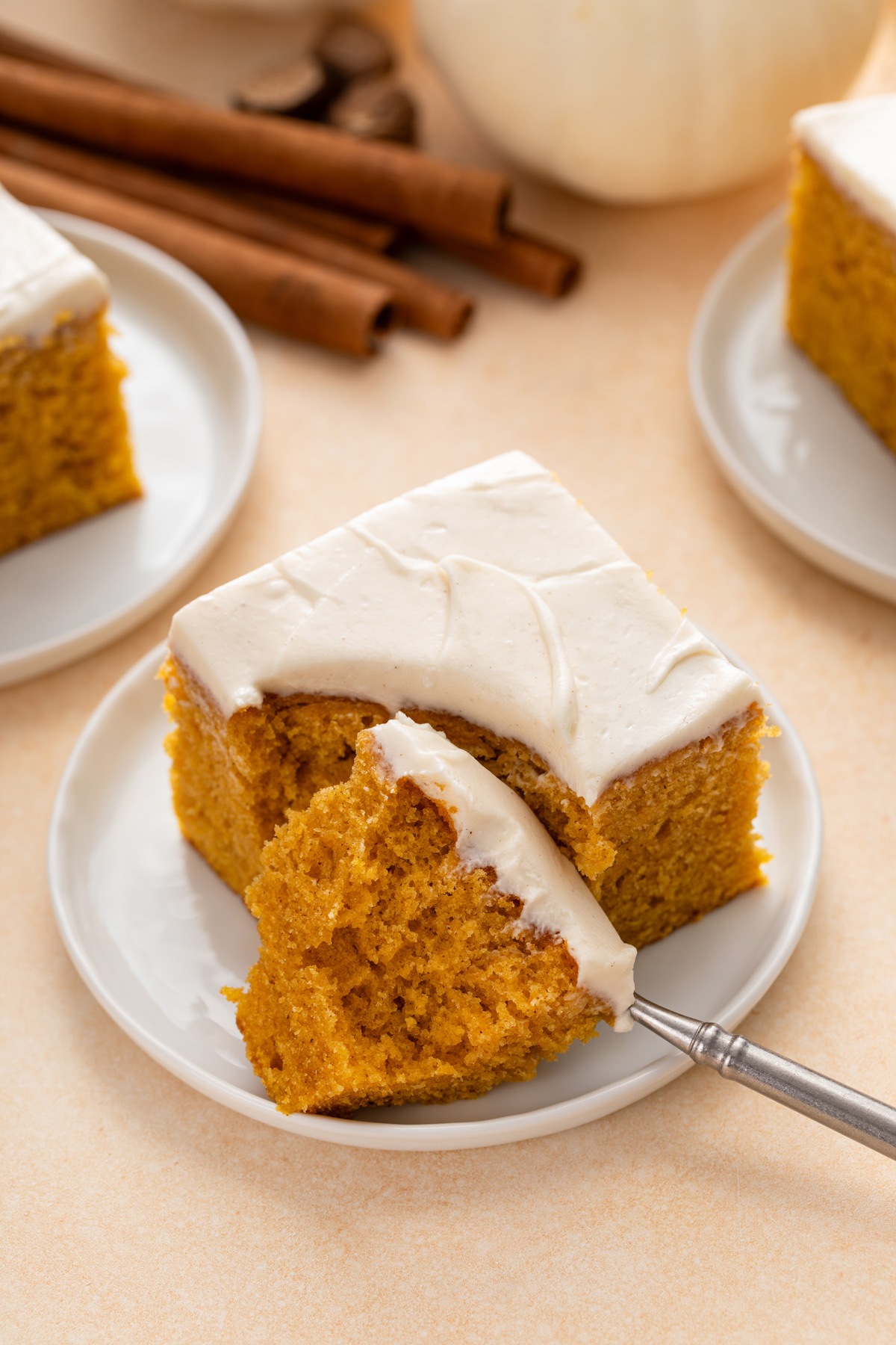 Fork cutting a bite from the corner of a slice of pumpkin cake on a white plate.