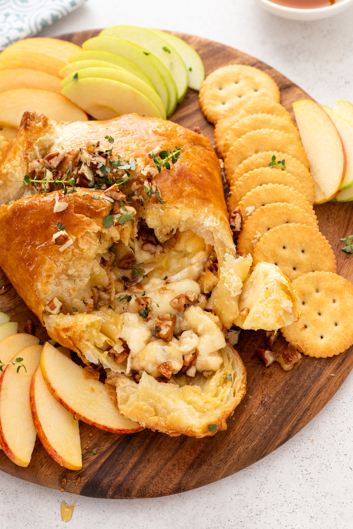 Baked brie in puff pastry that has been cut into surrounded by apple slices and crackers.