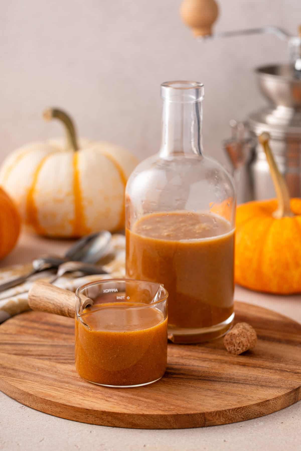 A bottle and a glass jar of pumpkin coffee syrup on a wooden board.