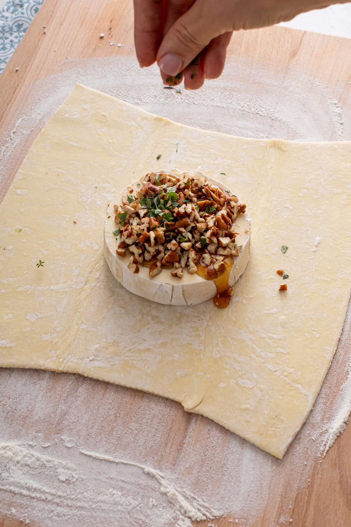 Brie topped with honey, pecans, and thyme set on a sheet of puff pastry.