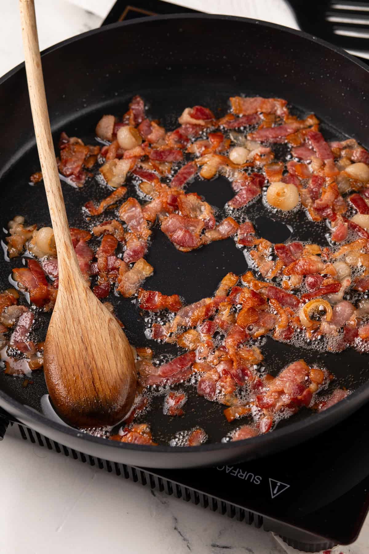 Bacon being cooked in a black skillet.