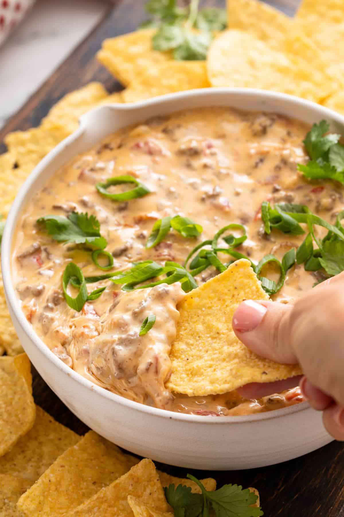 Hand dipping a tortilla chip into a bowl of rotel dip.