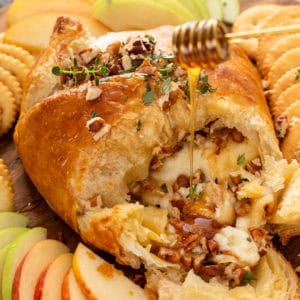 Honey being drizzled over baked brie in puff pastry.