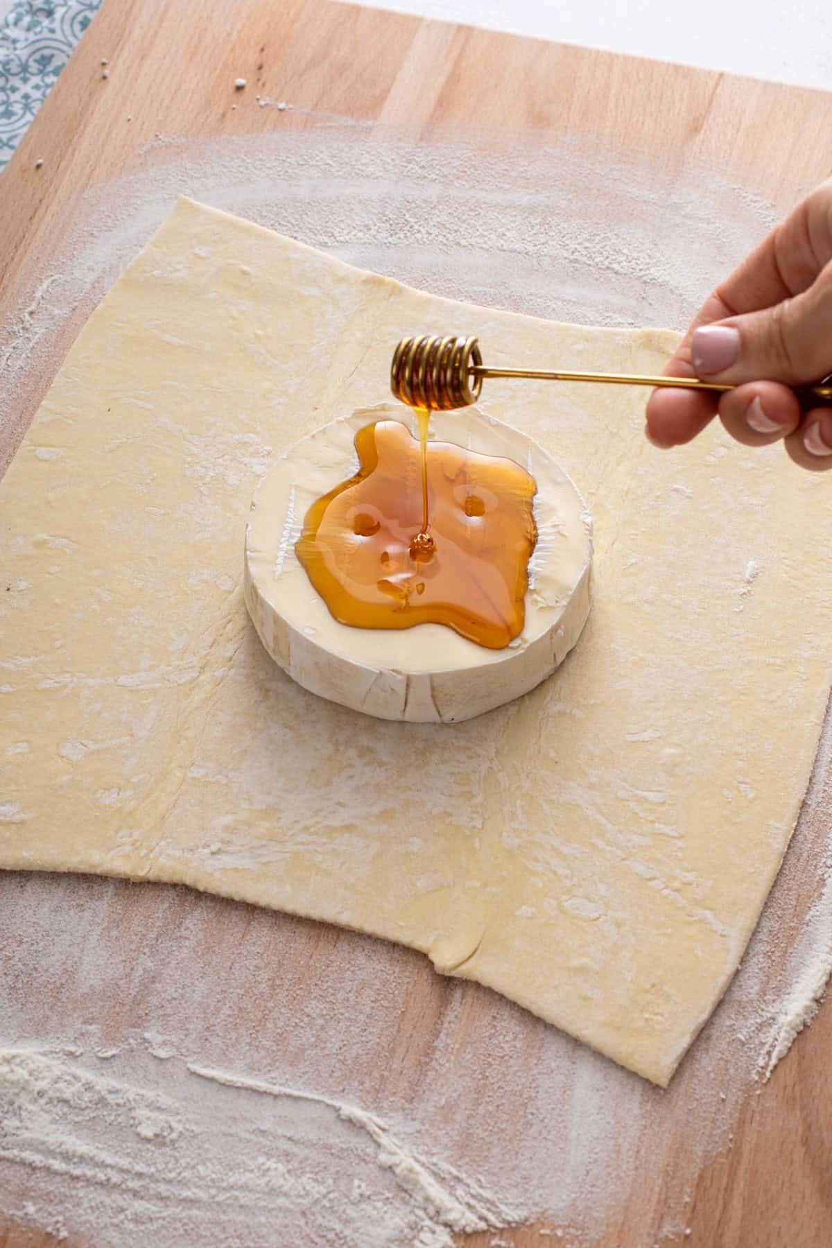 Honey being drizzled over brie set in the middle of a sheet of puff pastry.