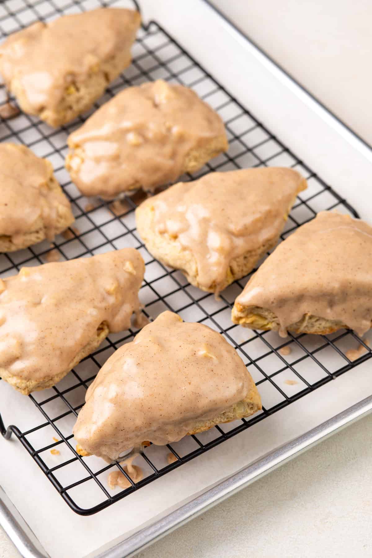 Glaze added to apple scones placed on a rack over a baking sheet.