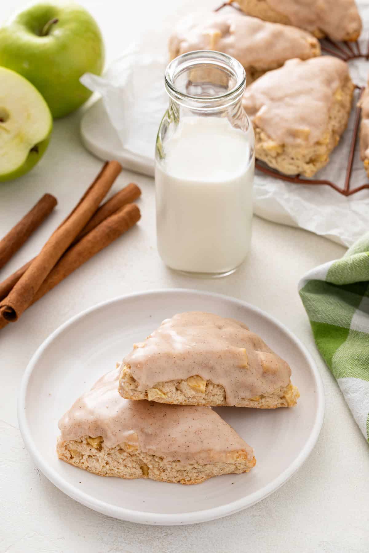 Two glazed apple scones on a white plate next to a glass of milk.