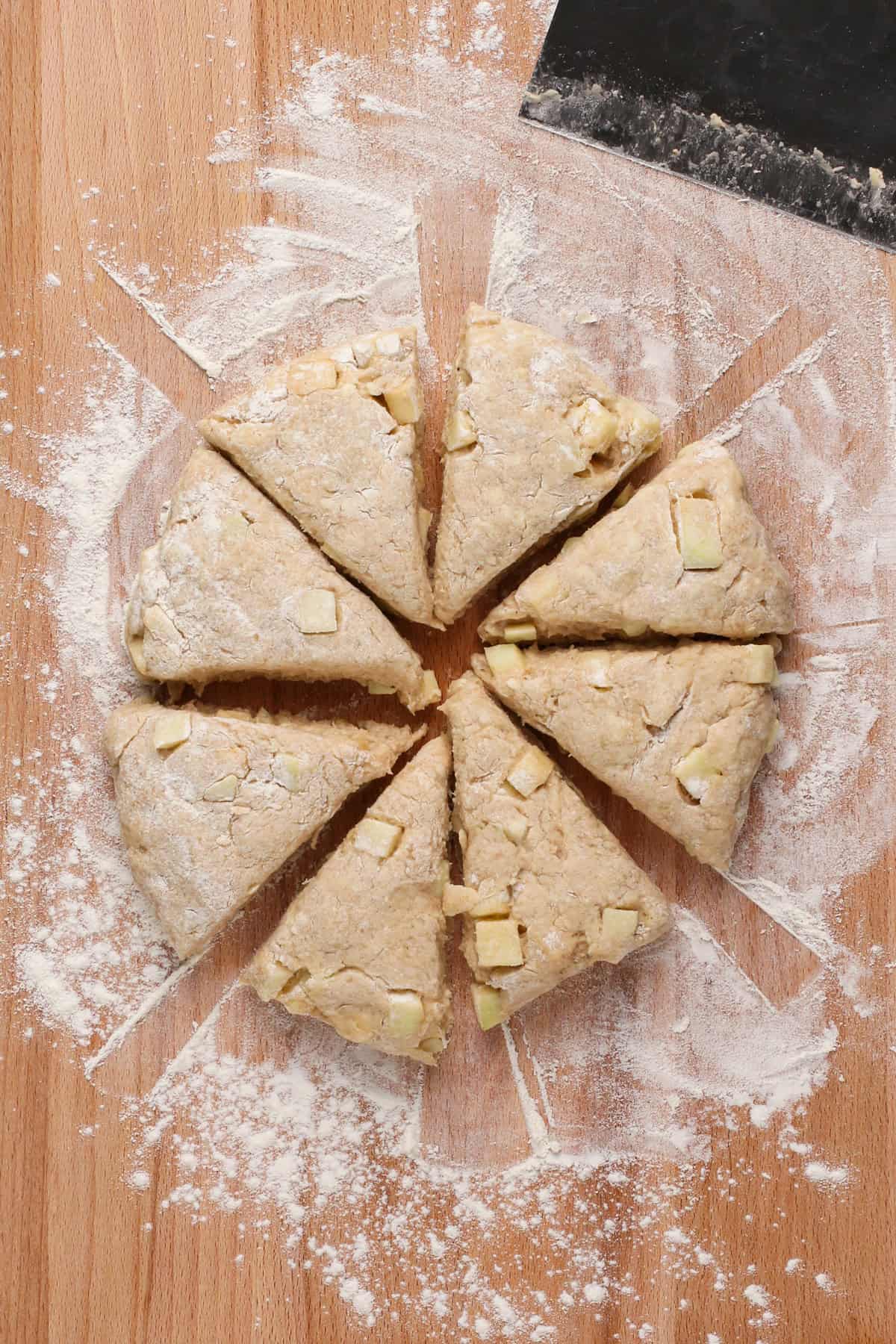 Circle of apple scone dough cut into triangles on a floured board.