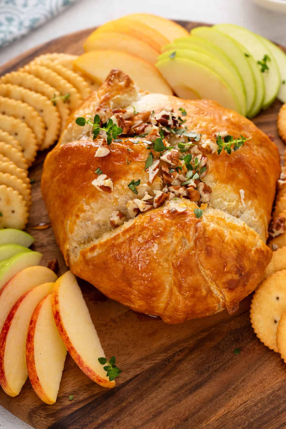 Close up of baked brie in puff pastry garnished with chopped pecans and thyme.