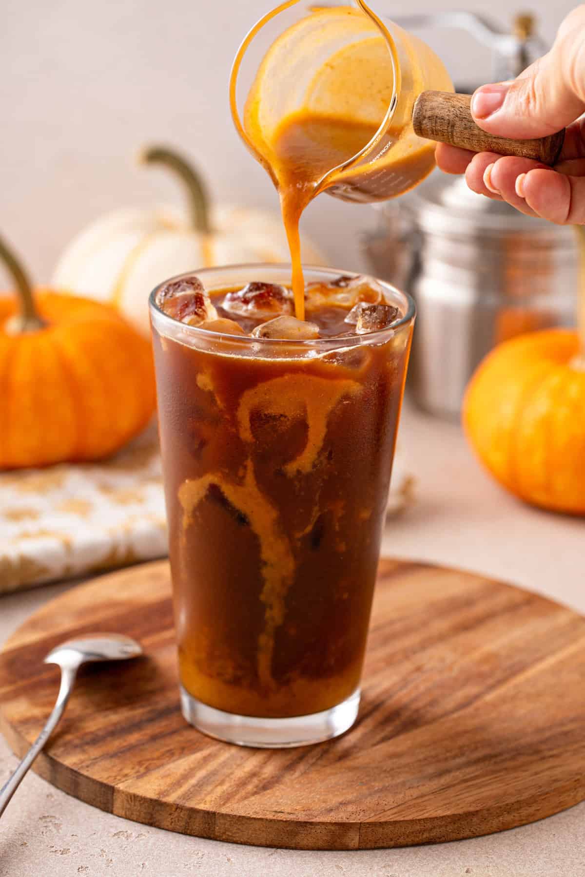 Pumpkin coffee syrup being poured into a glass of iced coffee.