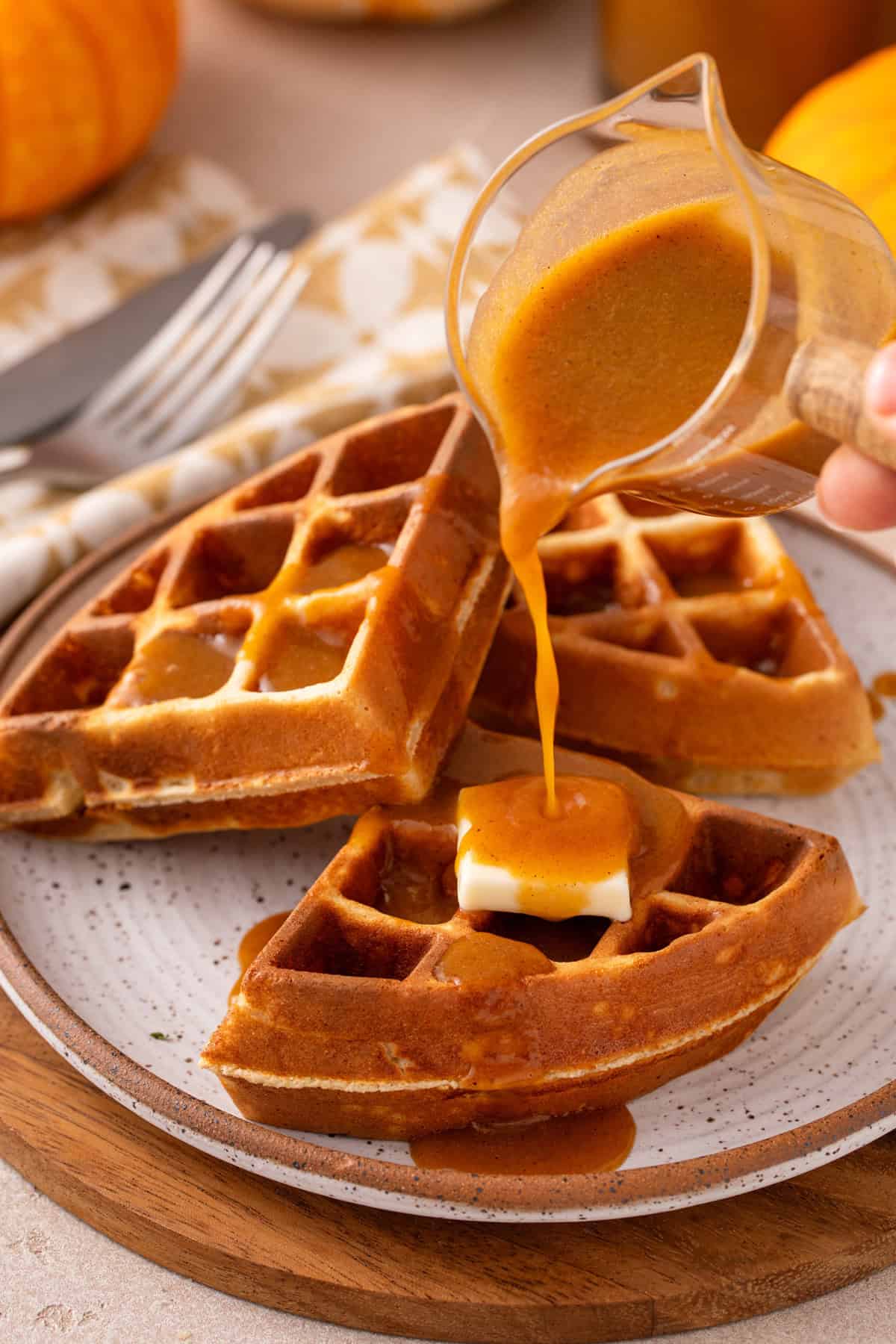 Pumpkin syrup being drizzled over waffles on a plate.