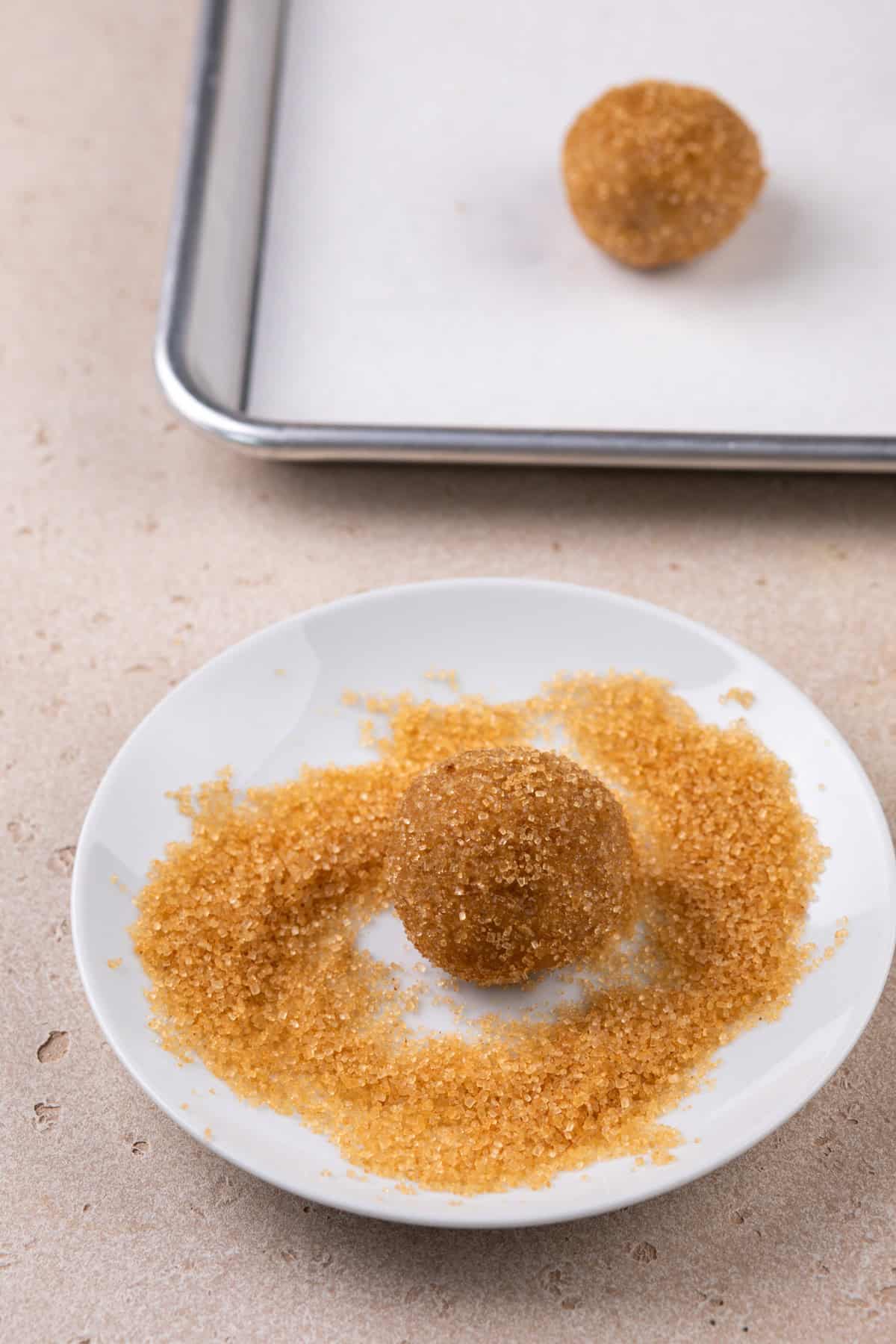 Ball of brown sugar cookie dough being rolled in turbinado sugar and cinnamon.