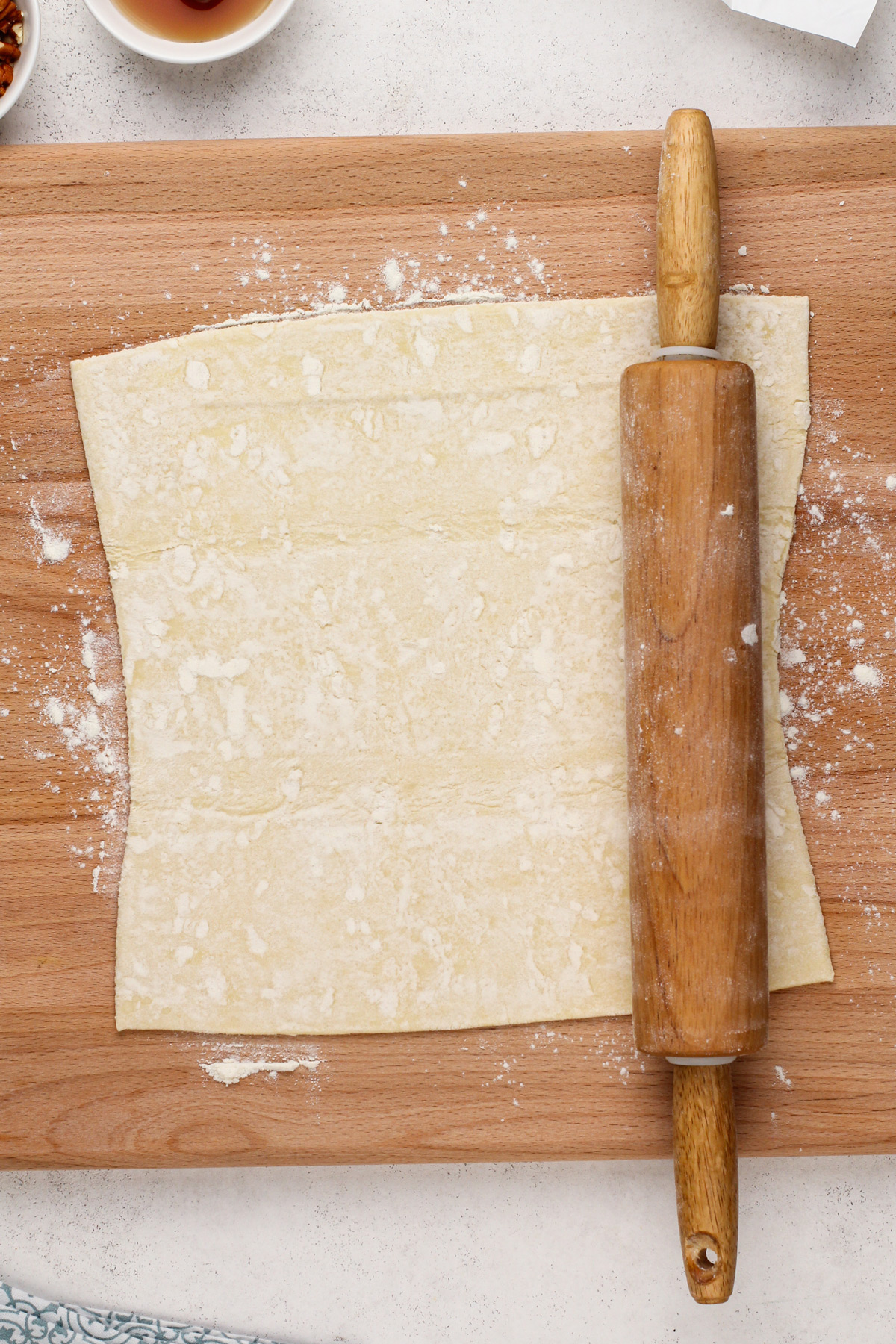 Rolling pin rolling out a sheet of puff pastry on a wooden board.