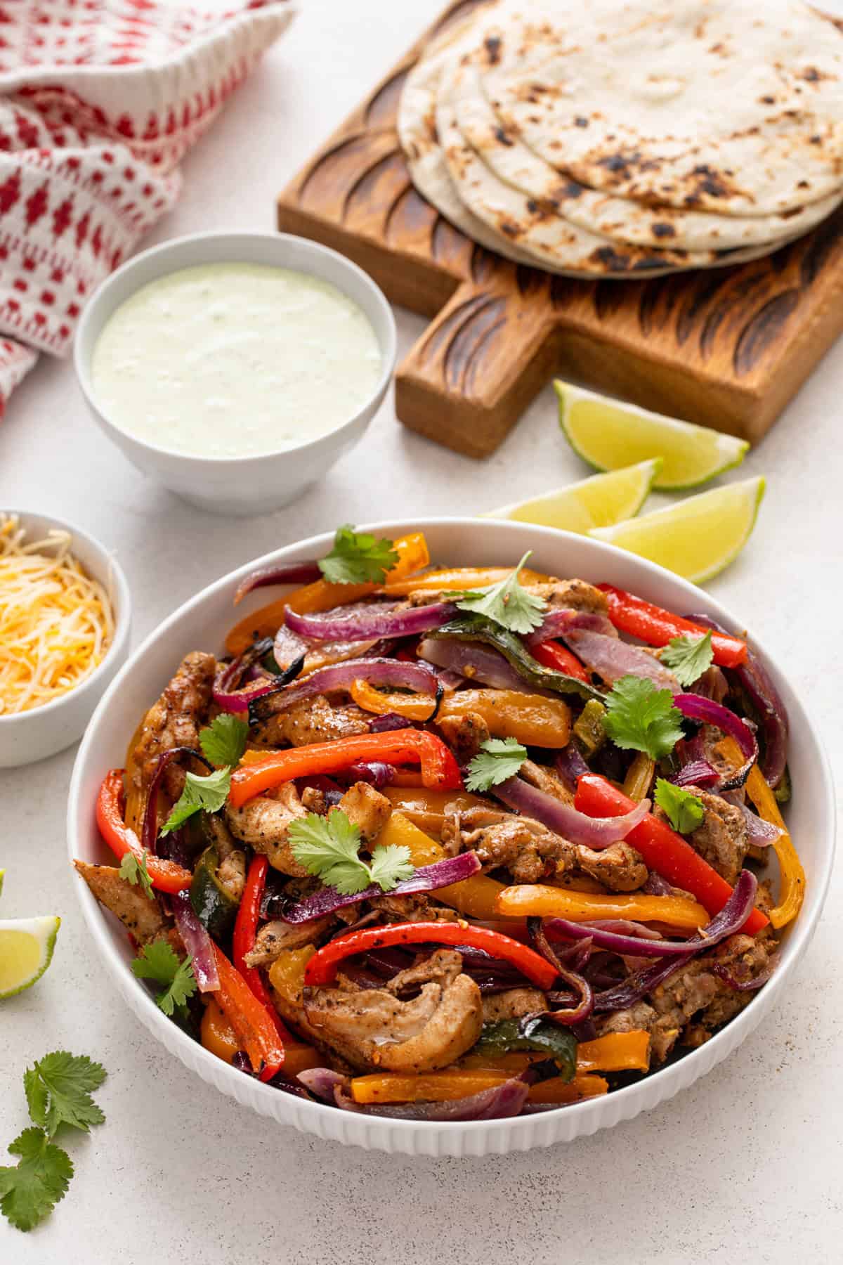 Bowl of sheet pan chicken fajitas on a countertop surrounded by fajita toppings.