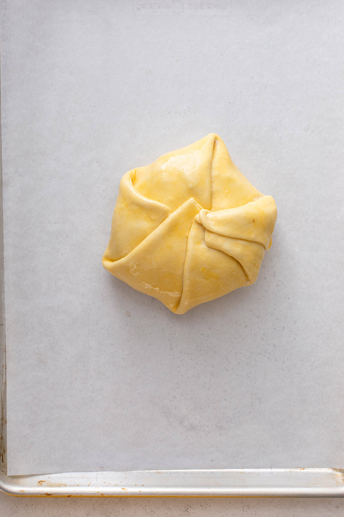 Brie wrapped in puff pastry and brushed with egg wash on a parchment-lined baking sheet.