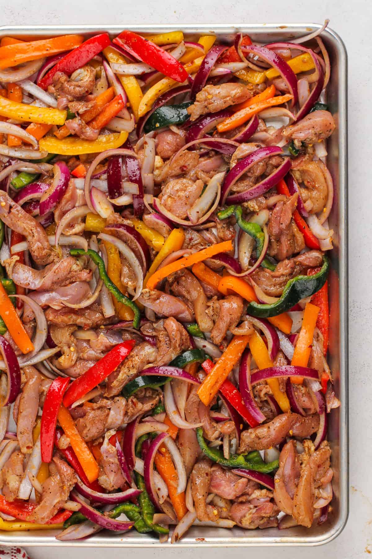 Sheet pan chicken fajita mixture spread on a baking sheet, ready to go in the oven.