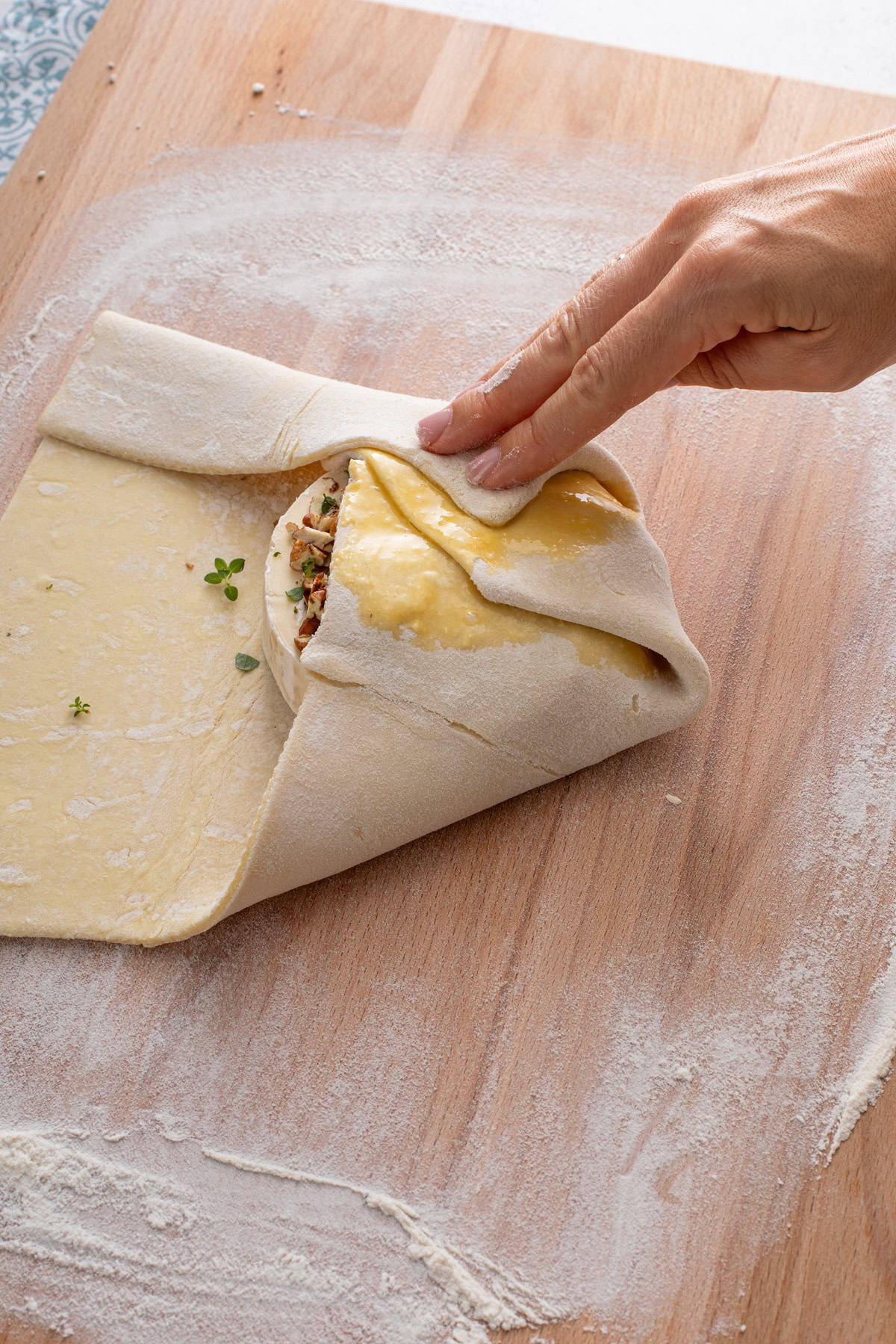 Puff pastry being folded over and around brie topped with honey and pecans.