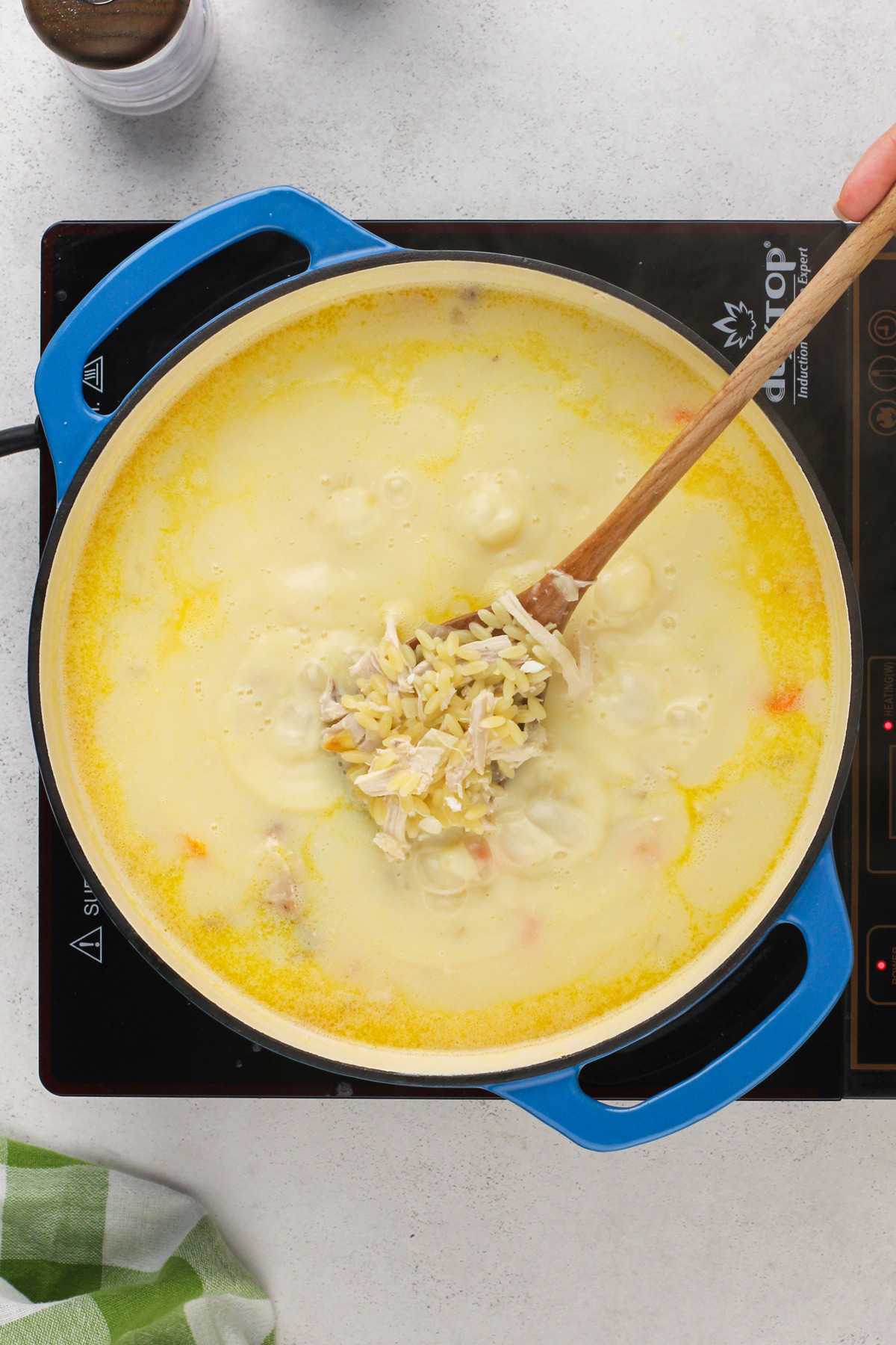 Spoon showing chicken and cooked orzo in a rich broth in a blue dutch oven.