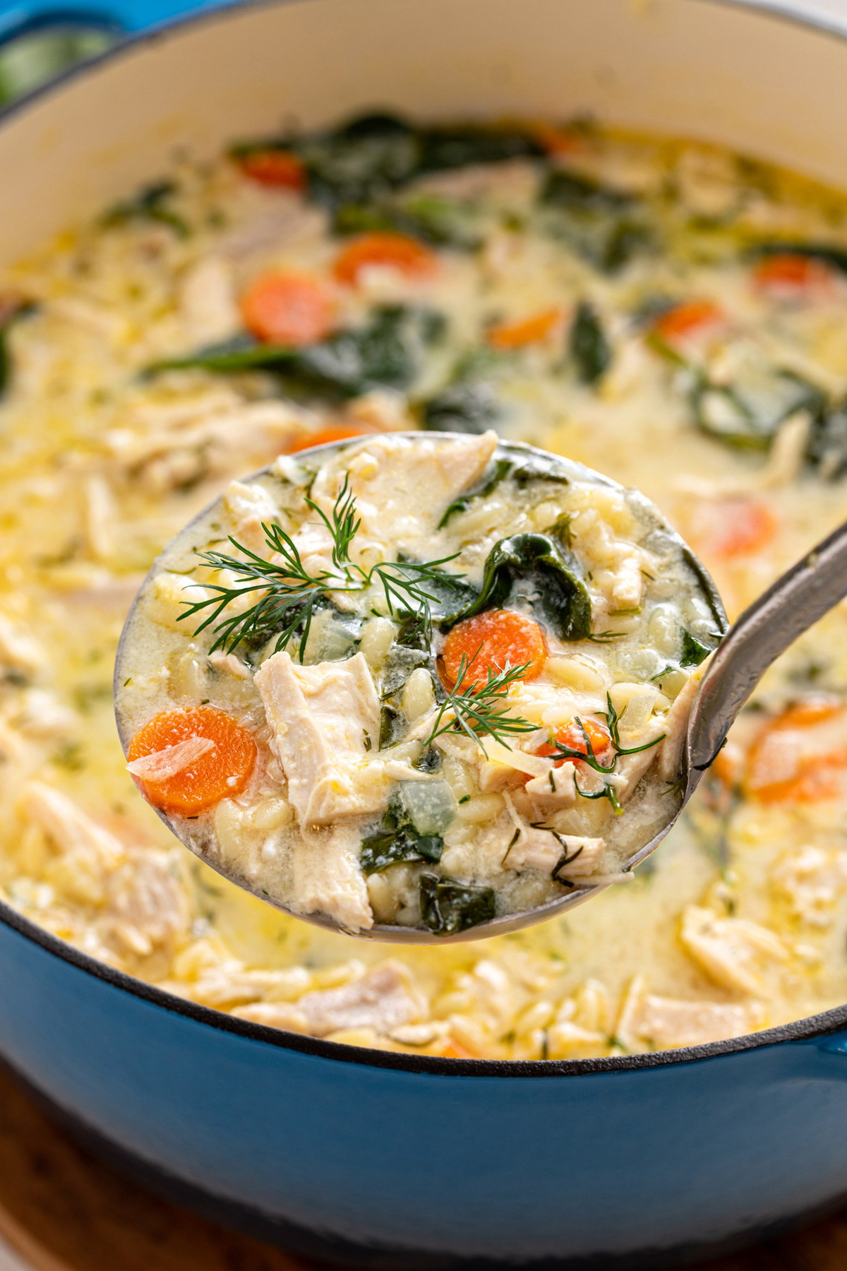 Ladle holding up a serving of lemon chicken orzo soup.