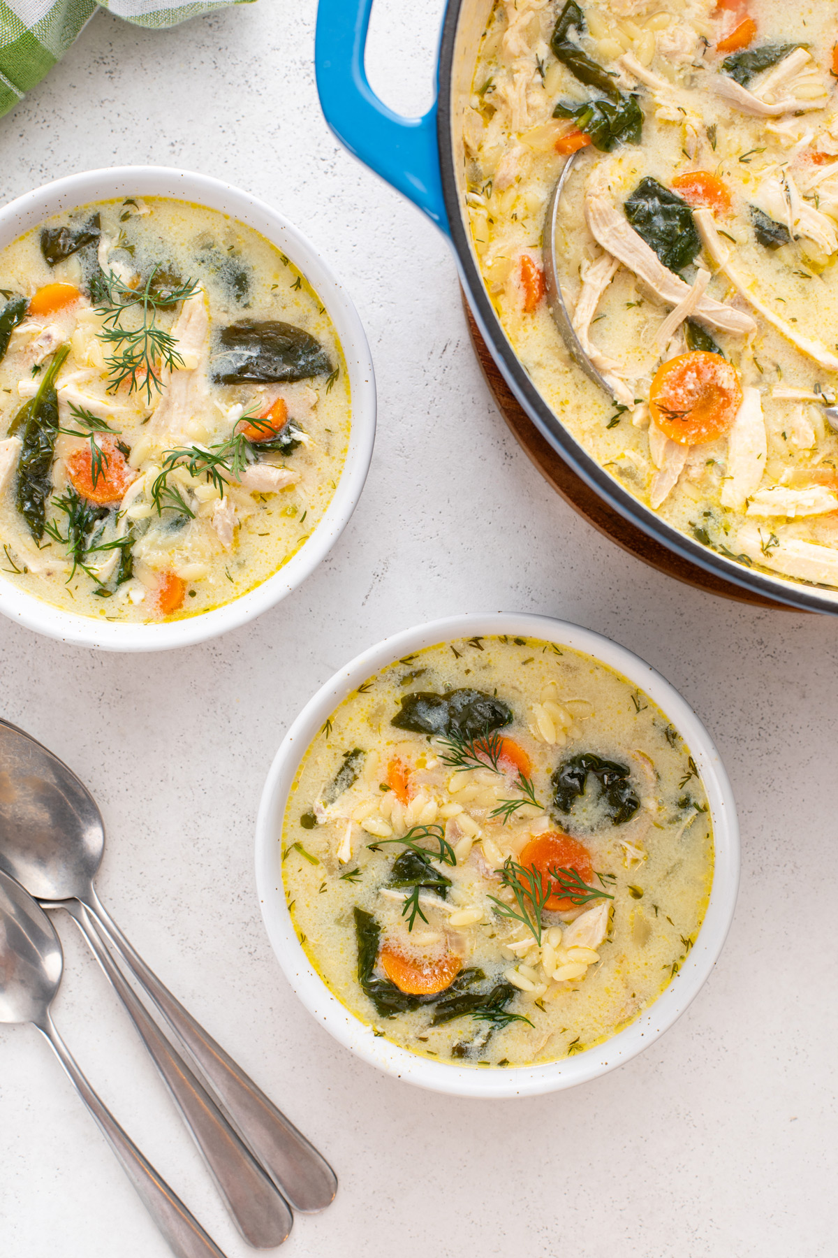 Overhead view of two bowls filled with lemon chicken orzo soup next to a pot of the soup.