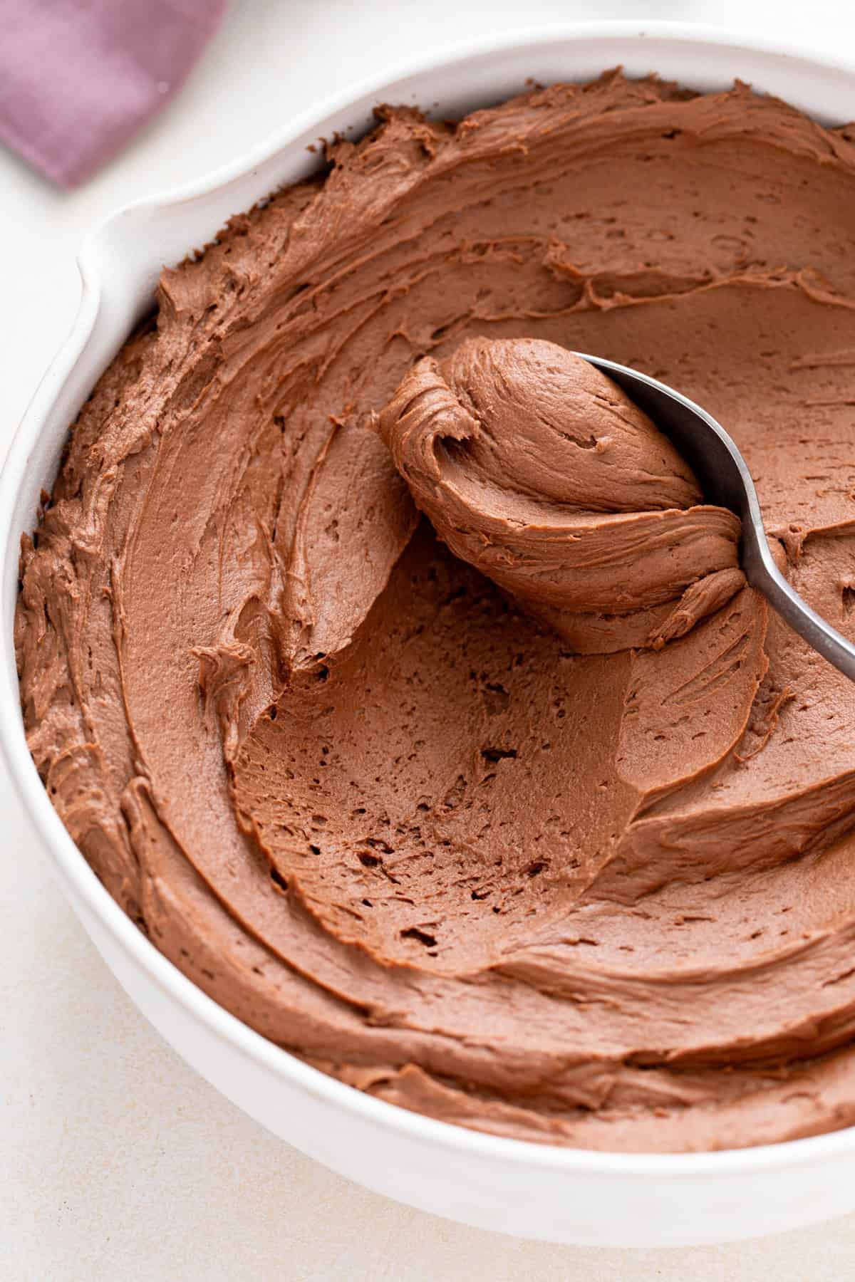 Spoon being run through a bowl of chocolate buttercream frosting.