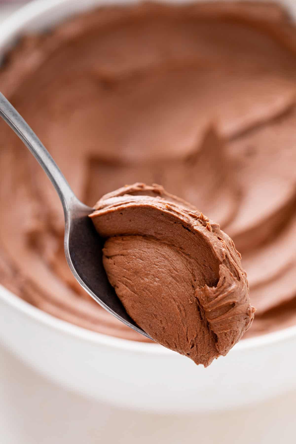 Spoonful of chocolate buttercream frosting being held up to the camera.