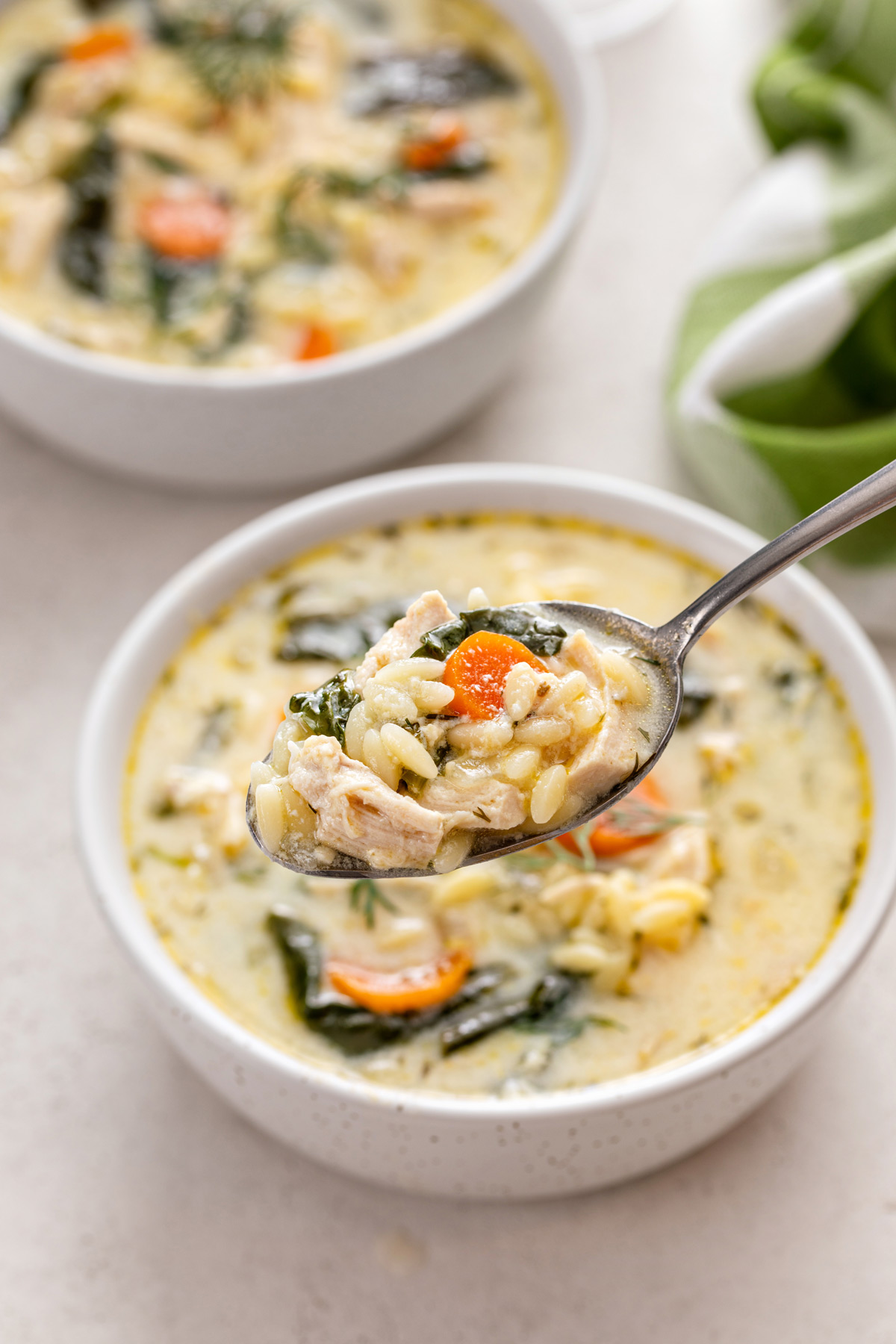 Spoon holding up a bite of lemon chicken orzo soup.