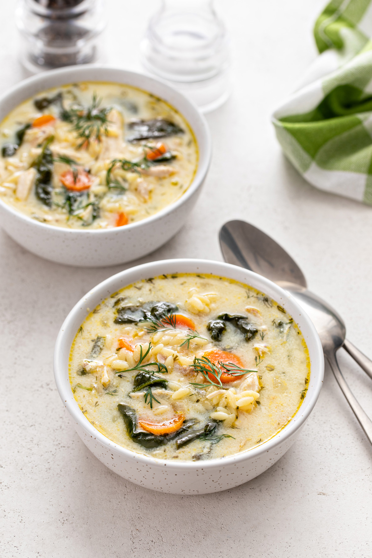 Two bowls filled with lemon chicken orzo soup next to spoons on a countertop.