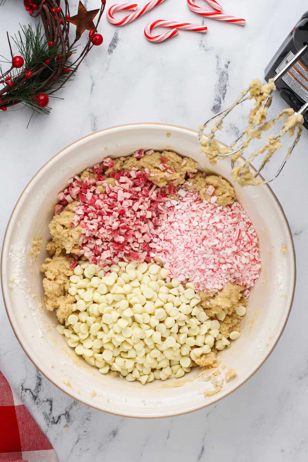 White chocolate chips and peppermint candies added to cookie dough in a bowl.