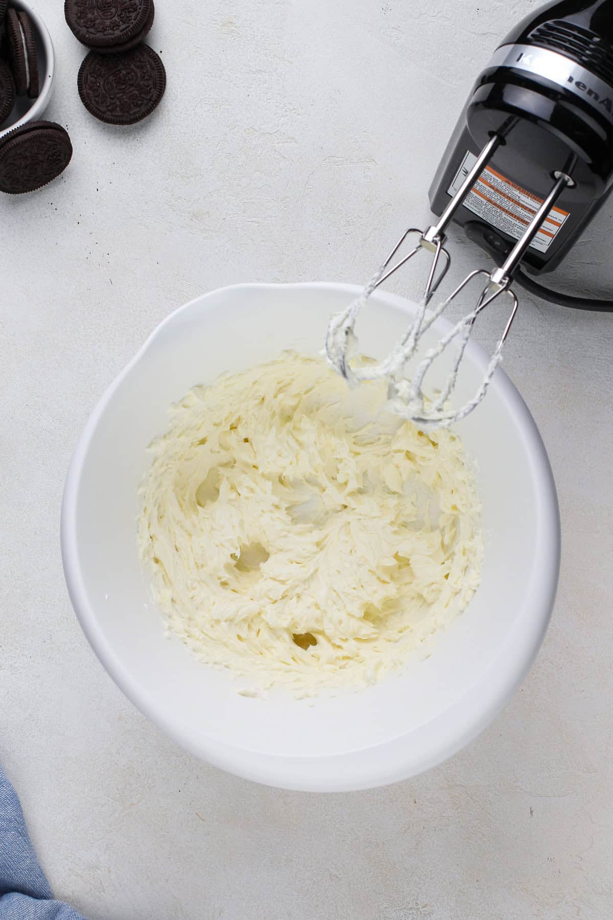 Cream cheese beaten with a hand mixer in a white bowl.