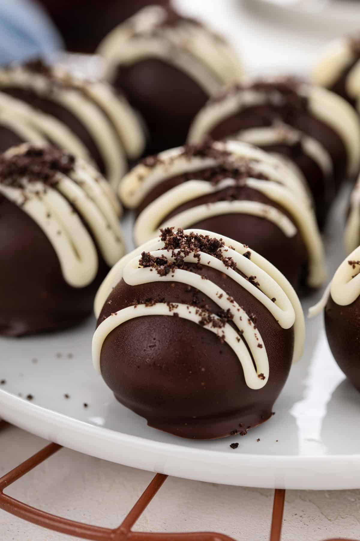 Close up of Oreo truffles drizzled with white chocolate and topped with oreo crumbs on a white plate.