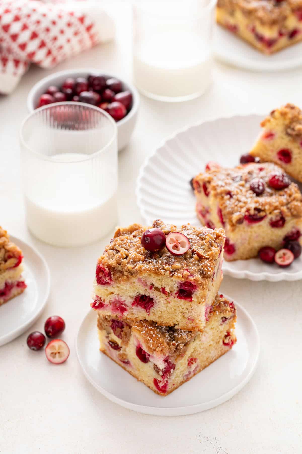 Two white plates of cranberry cake next to a glass of milk.