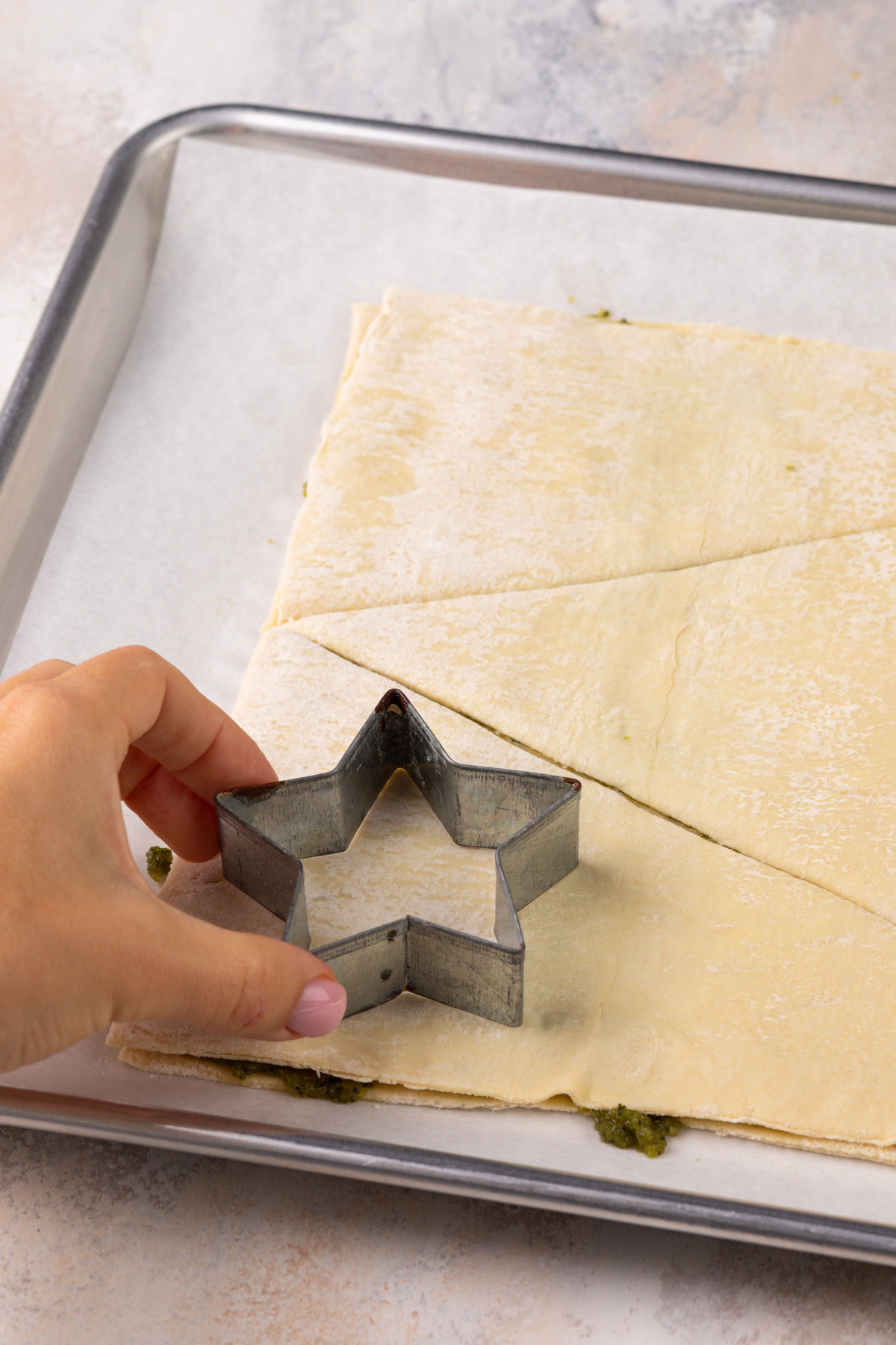 Hand using a star cookie cutter to cut out a star from puff pastry.