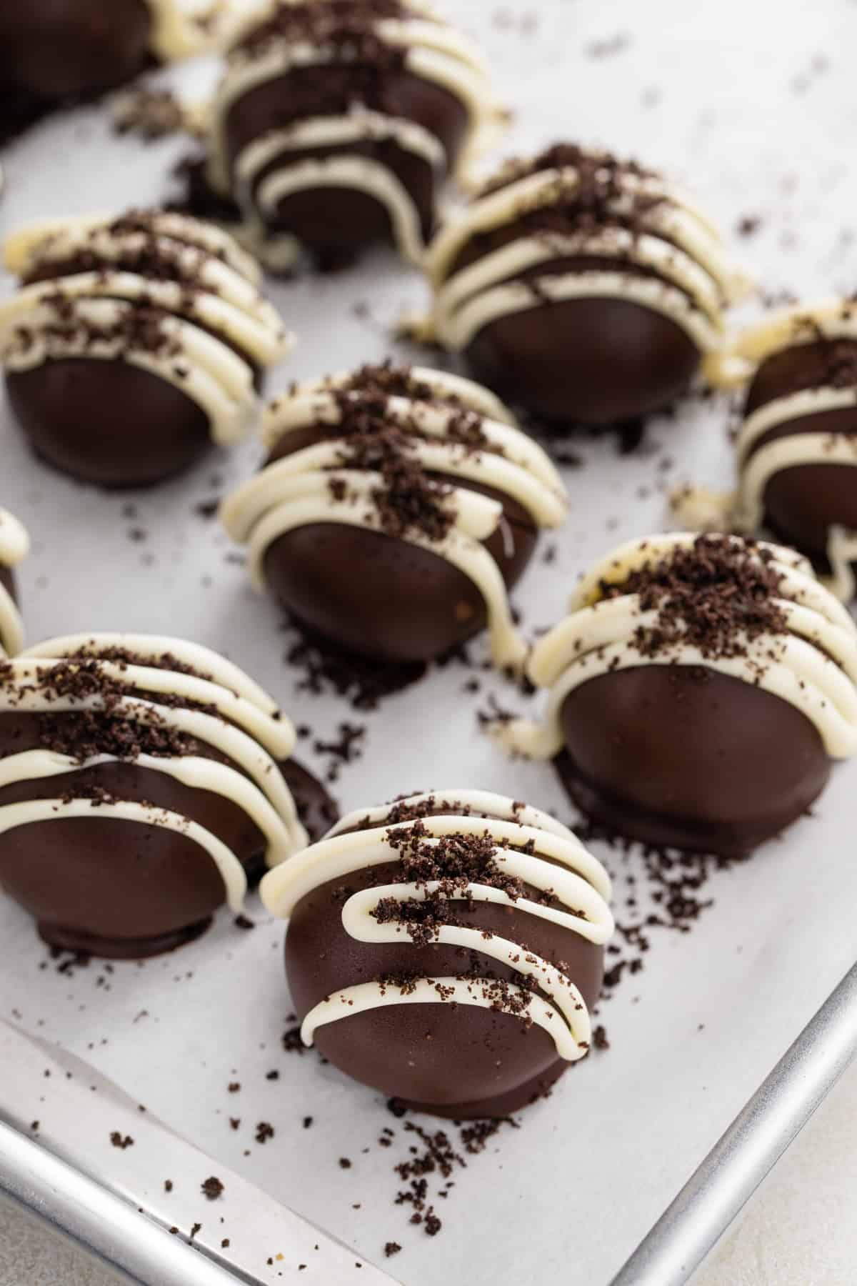 Oreo truffles on a lined baking sheet decorated with white chocolate and oreo crumbs.