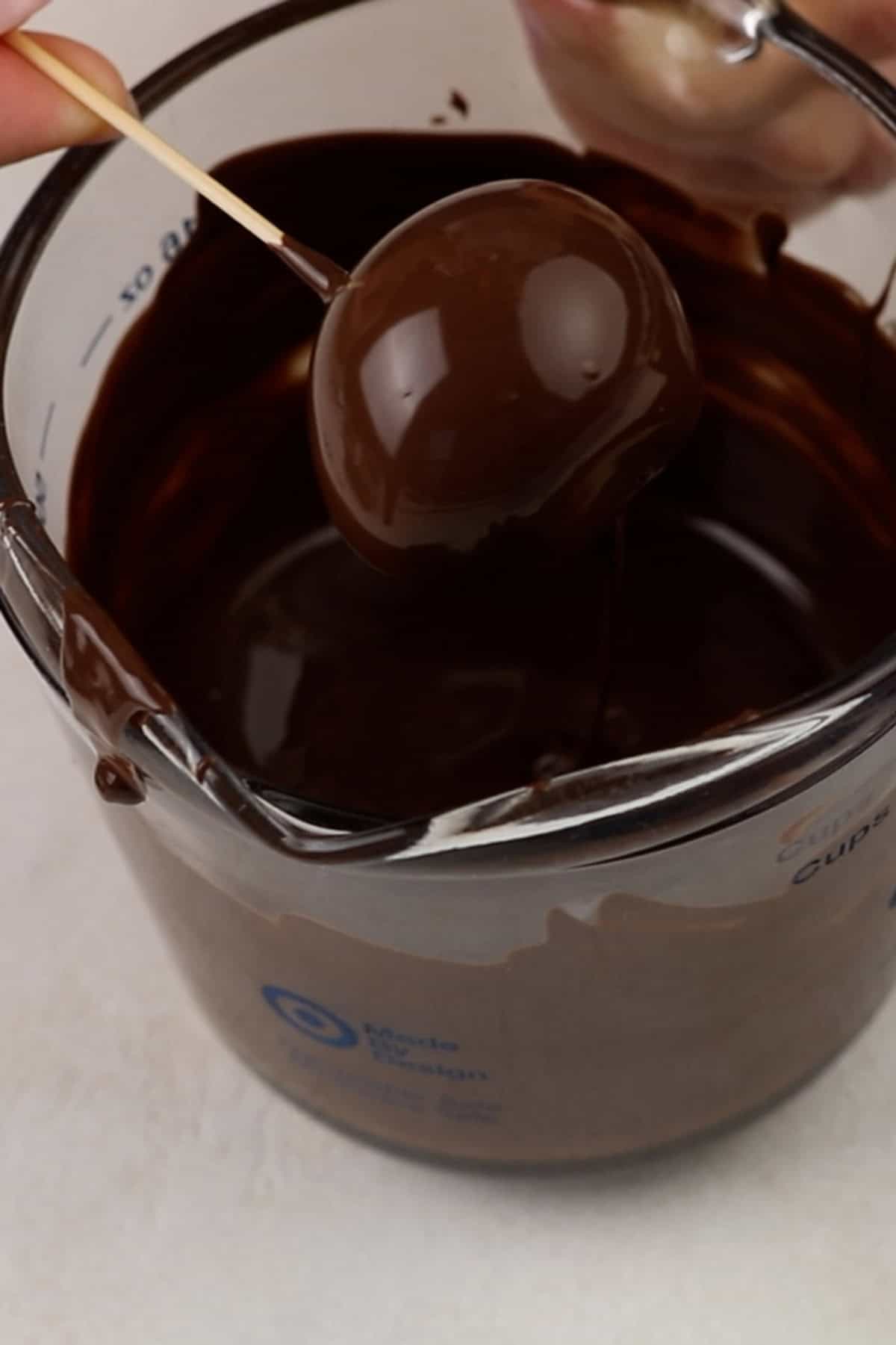 Oreo ball dipped in melted chocolate held over the measuring cup of chocolate.