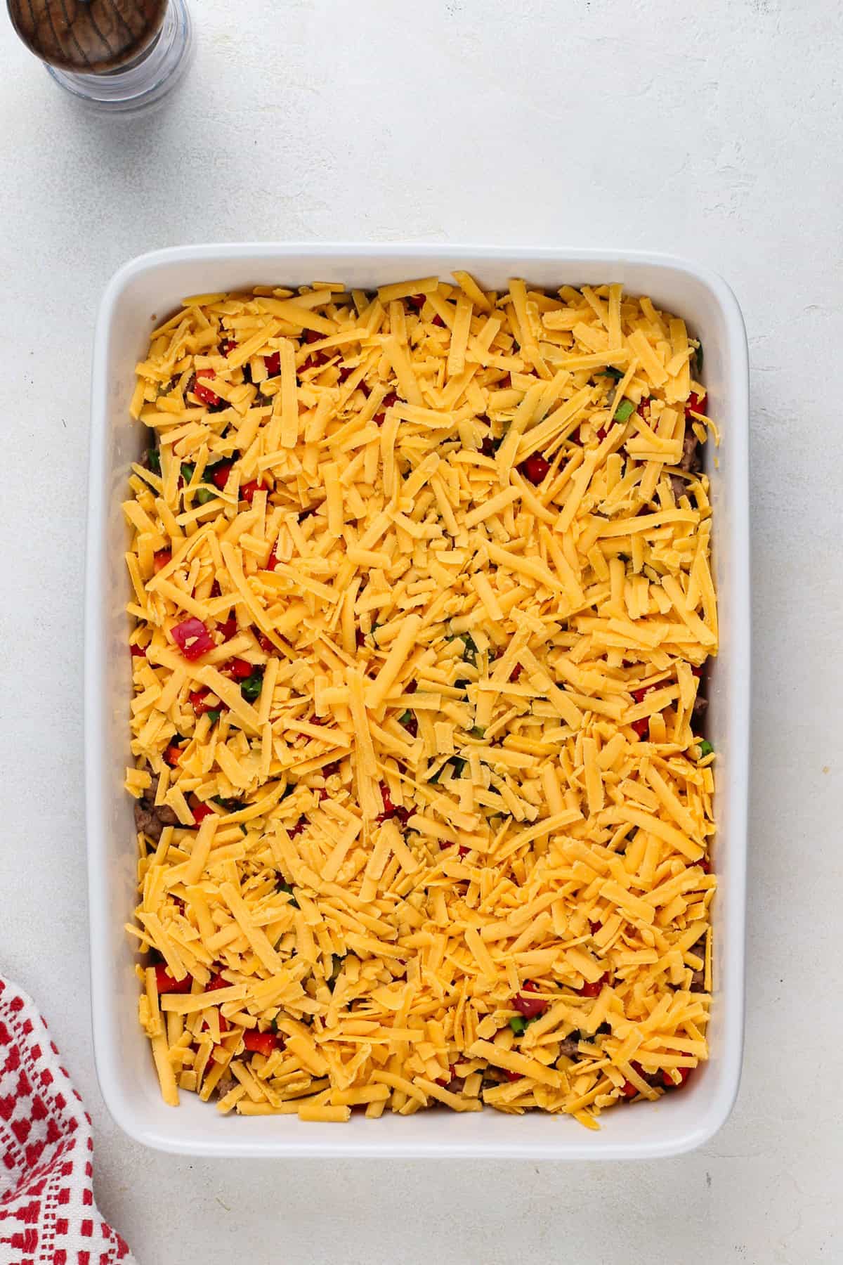 Sausage, peppers, and cheese layered in a baking dish for breakfast casserole.